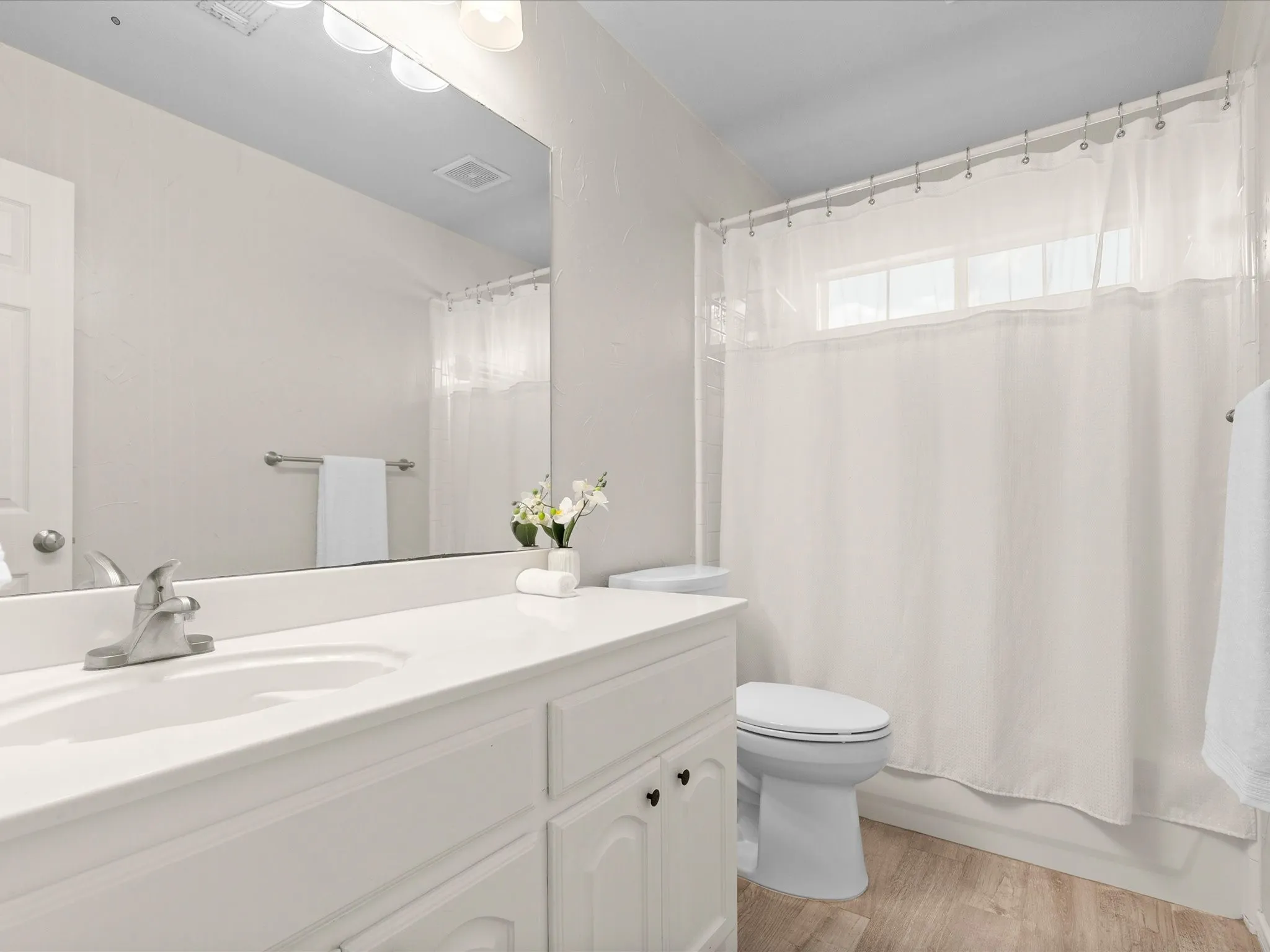 White vanity with integrated sink, brushed nickel faucet, large wall mirror, and wood-finish flooring