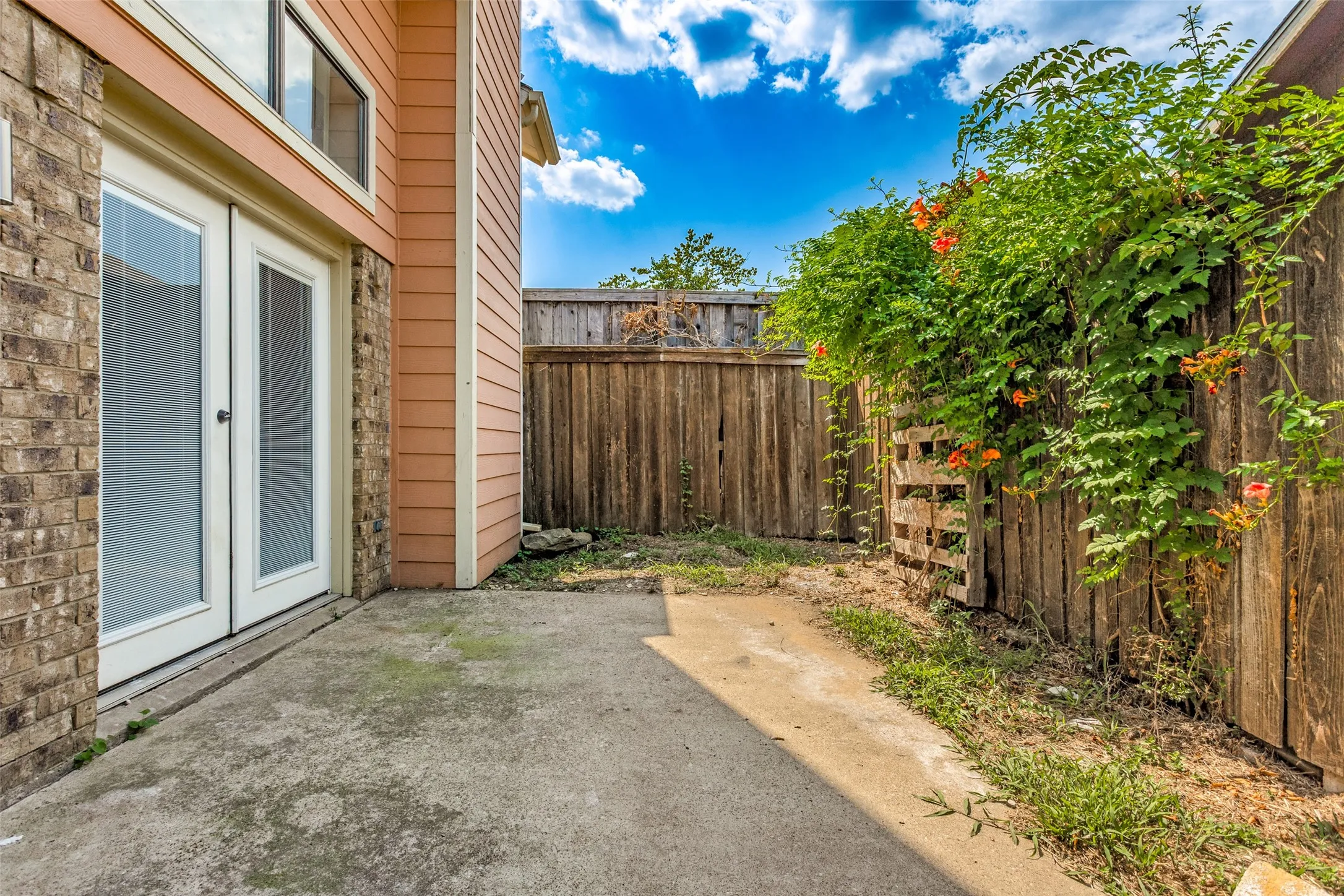 Concrete patio with brick and siding exterior, double glass panel doors, and a wood privacy fence