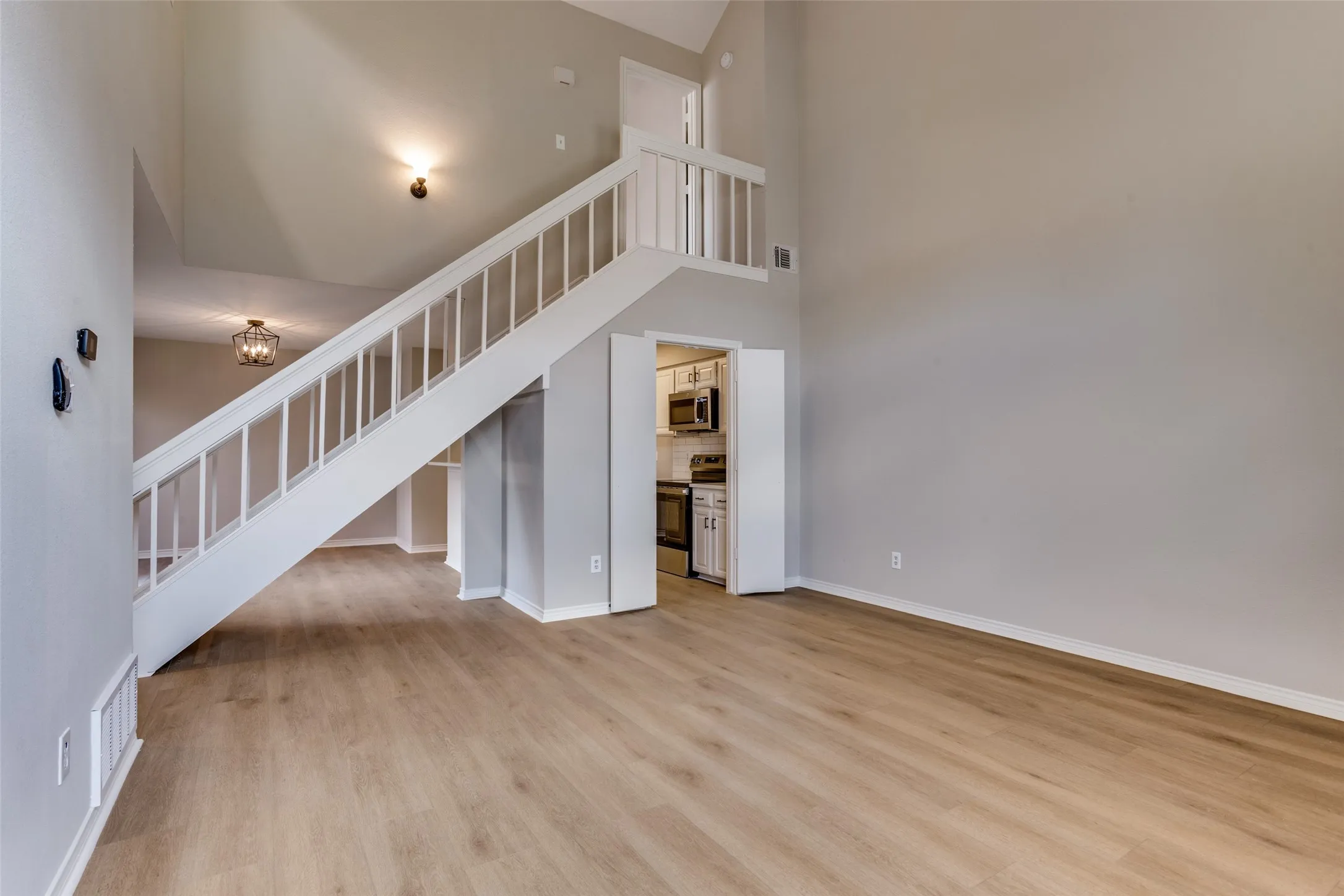 Vaulted ceiling, wood-finish flooring, white staircase with balusters, recessed lighting, and kitchen access