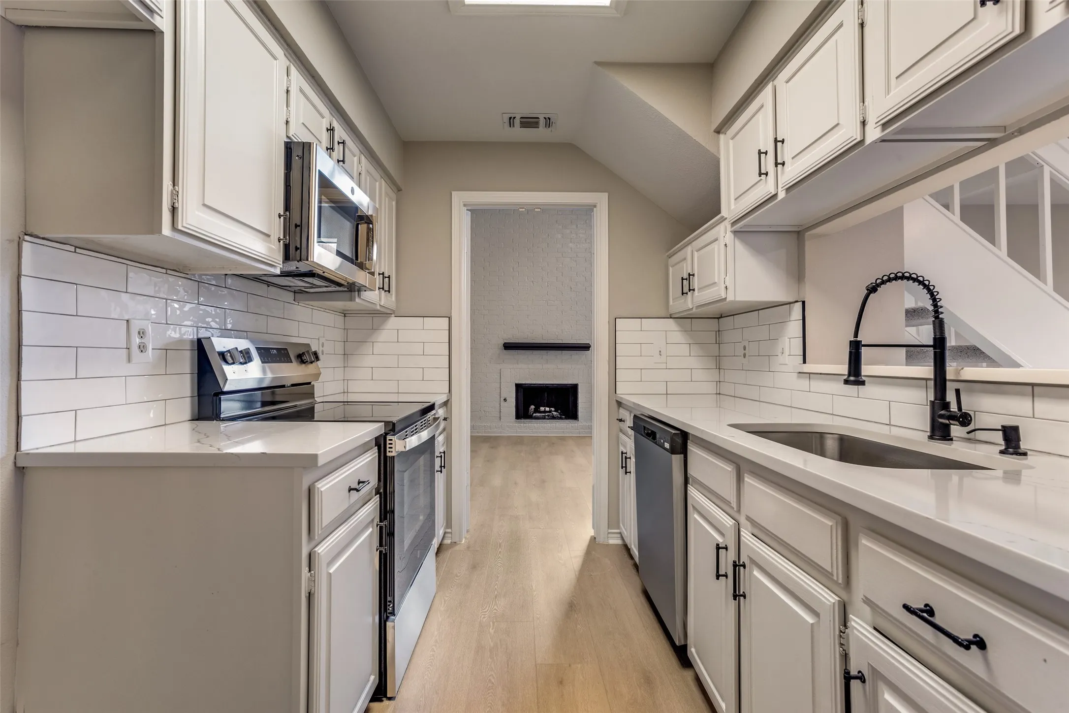 Galley kitchen featuring white cabinetry, subway tile backsplash, light countertops, stainless steel appliances, and a stainless steel sink with a black pull-down faucet