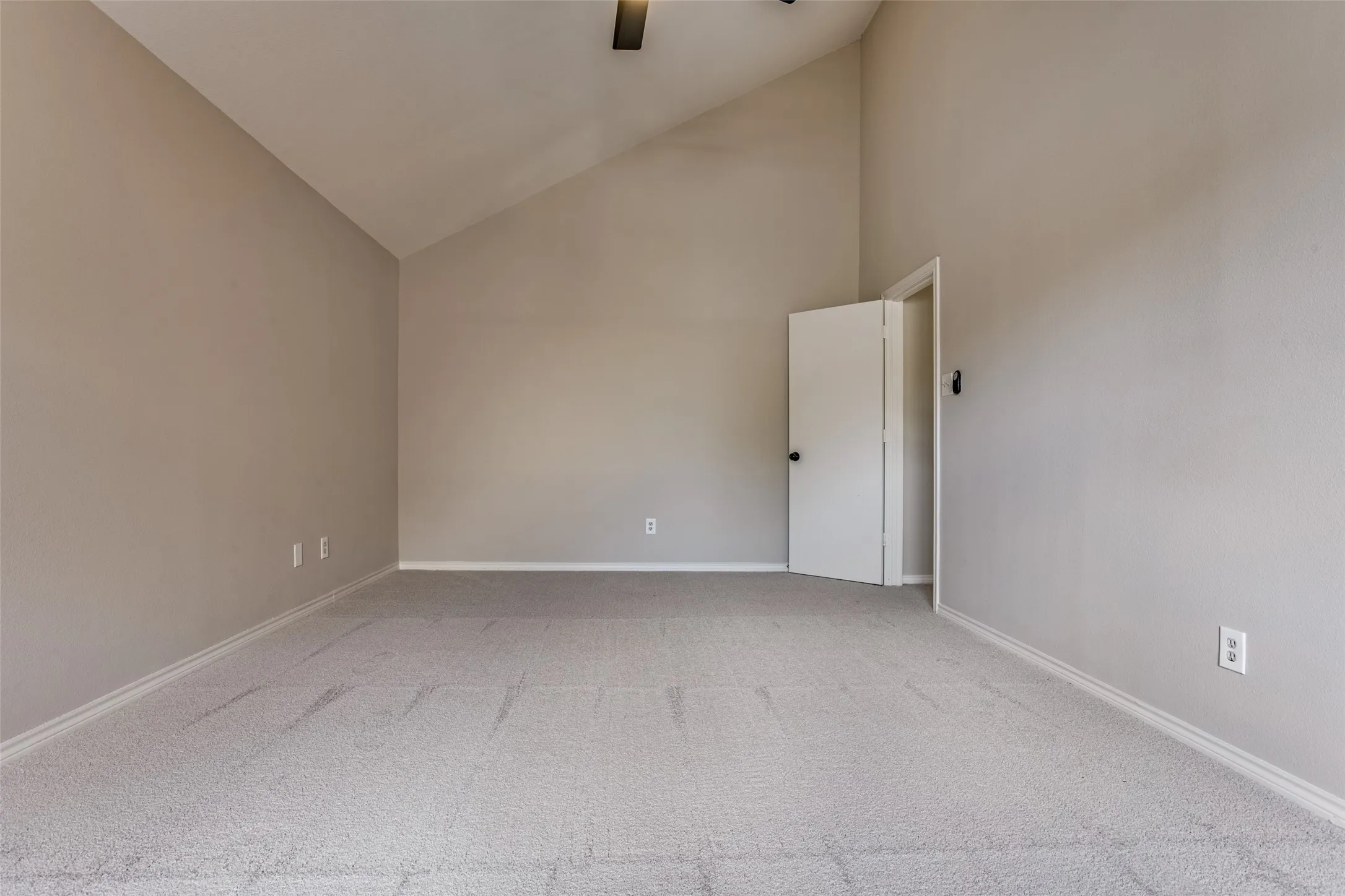 Vaulted ceiling, neutral wall paint, light-toned carpeting, white trim, and a ceiling fan