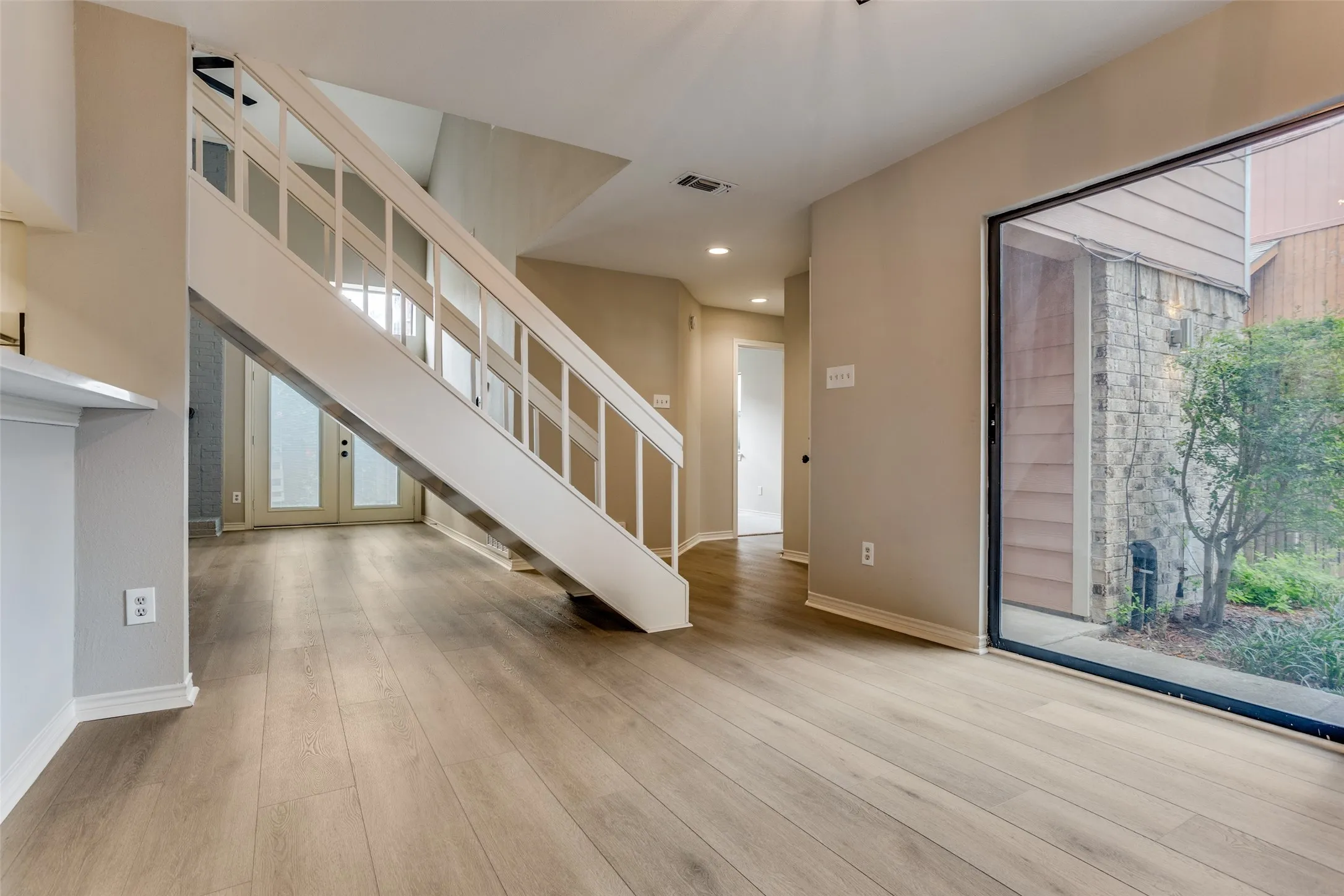 Wood-finish flooring, white staircase with balusters, built-in shelving, sliding glass door, and stone exterior wall