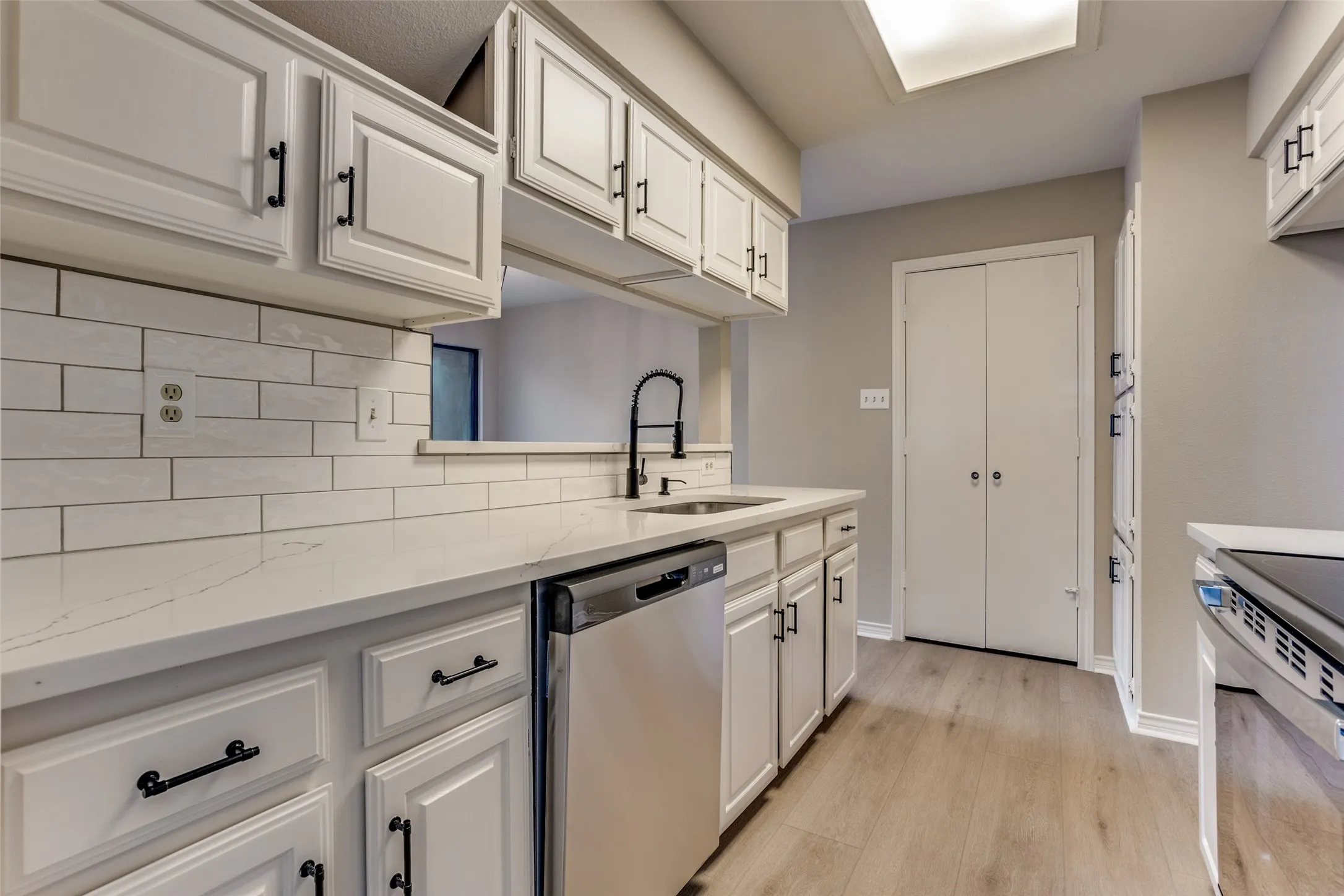 Kitchen featuring white cabinetry, subway tile backsplash, light-toned wood-finish flooring, and a stainless steel dishwasher