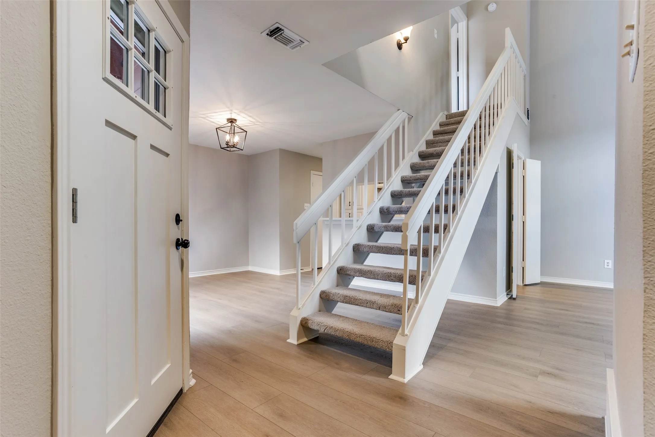 Entryway featuring wood-finish flooring, a modern chandelier, and a carpeted staircase with white balusters