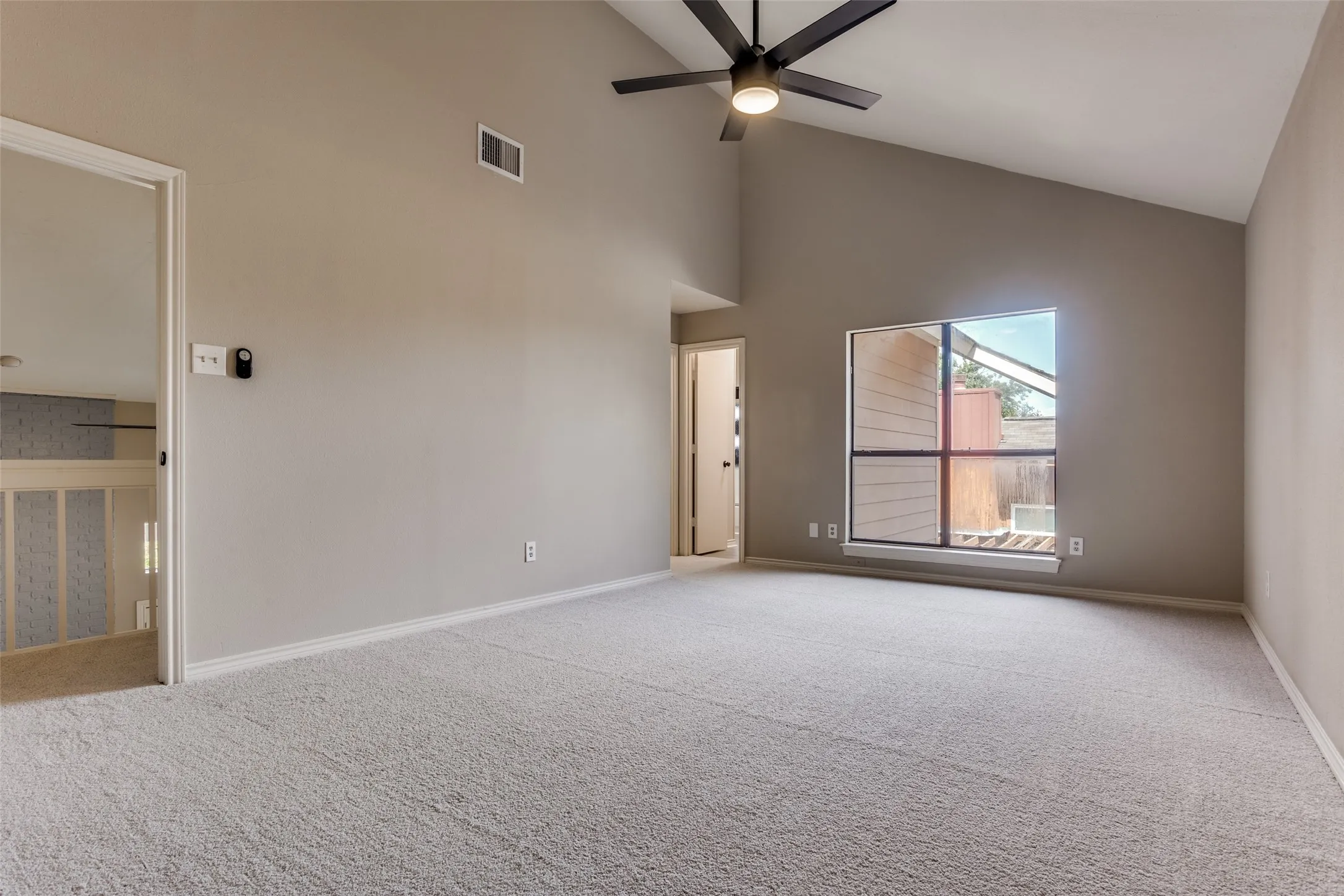 Spacious room with vaulted ceilings, a prominent window, ceiling fan with integrated lighting, and neutral-toned carpeting