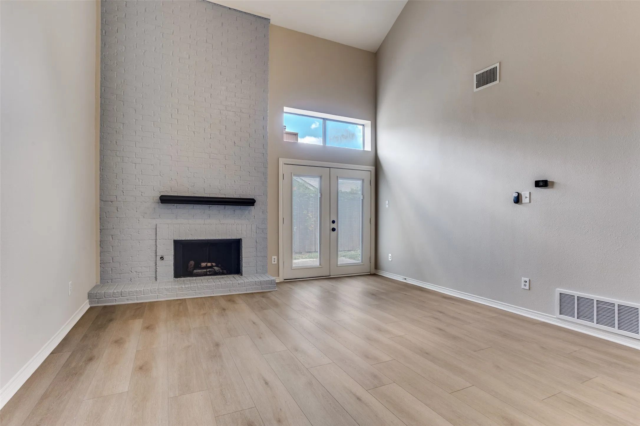 Vaulted ceiling, brick fireplace with mantel, wood-finish flooring, and double doors with transom window