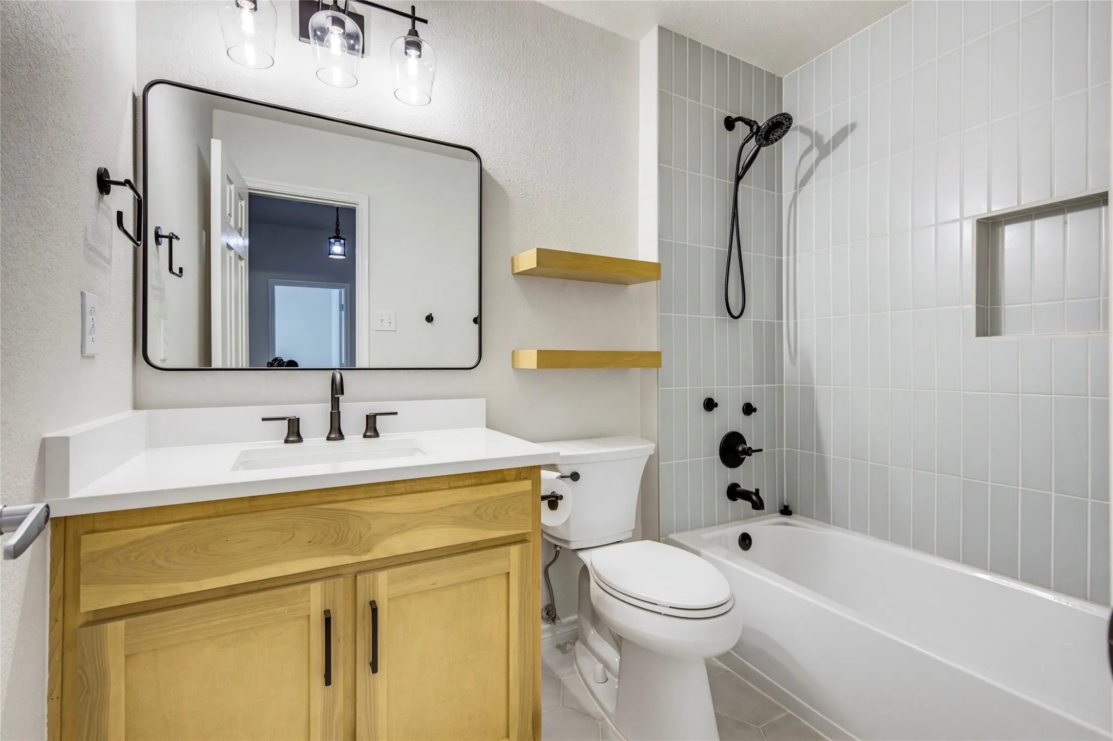 The updated upstairs bath features a warm wood vanity, matte black fixtures, and a tiled tub-shower combo.
