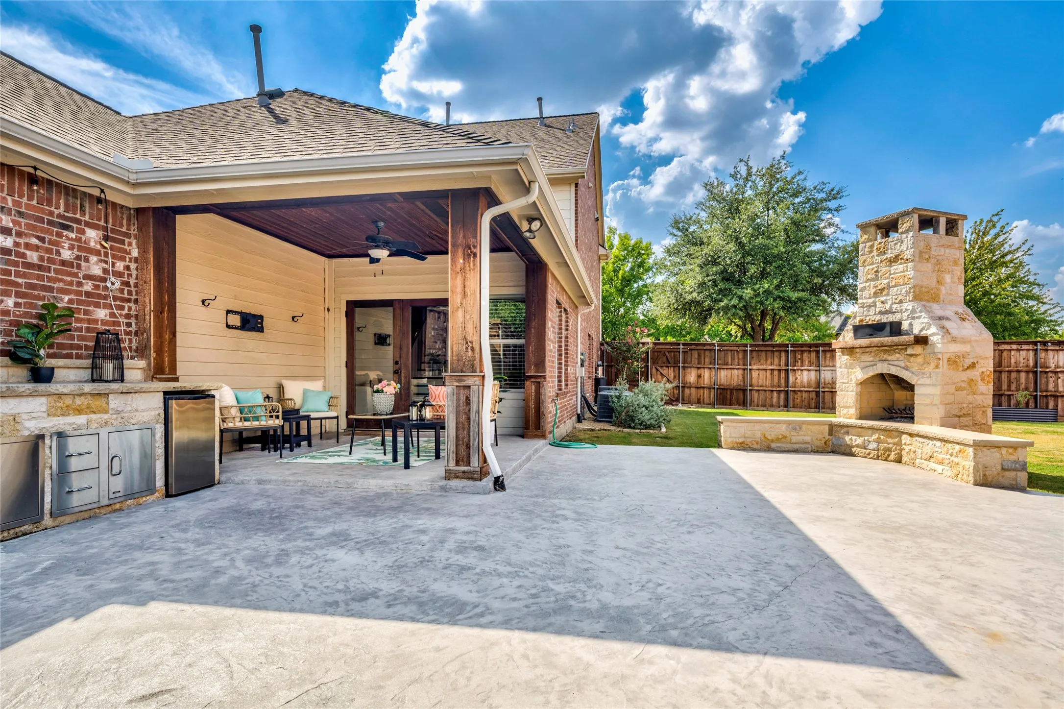 The covered patio steps out to an extended patio anchored by a brick fireplace with wraparound stone-wall seating.
