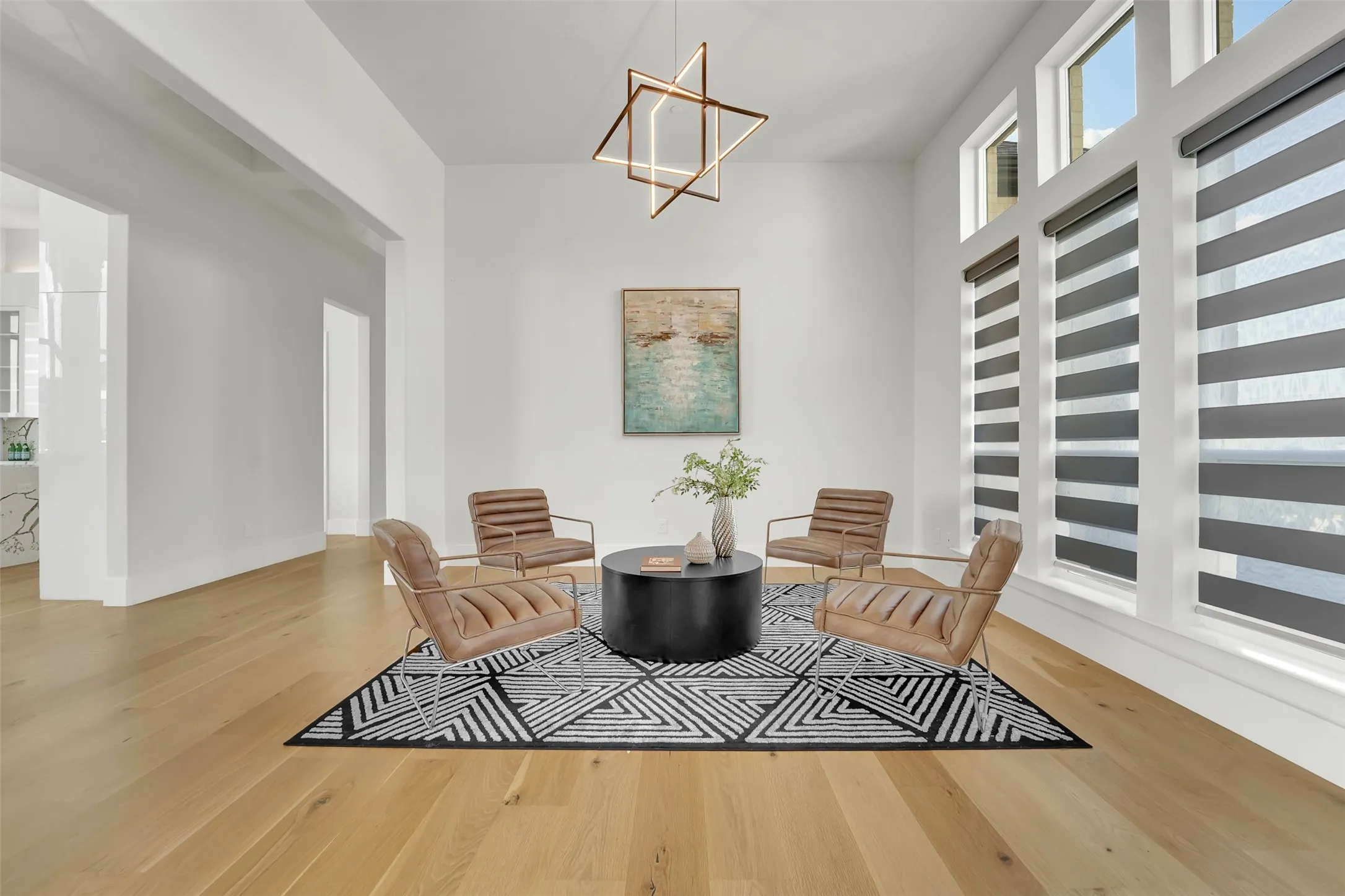 High ceilings, wood-finish flooring, abundant natural light from large windows, modern geometric chandelier, and crisp white walls