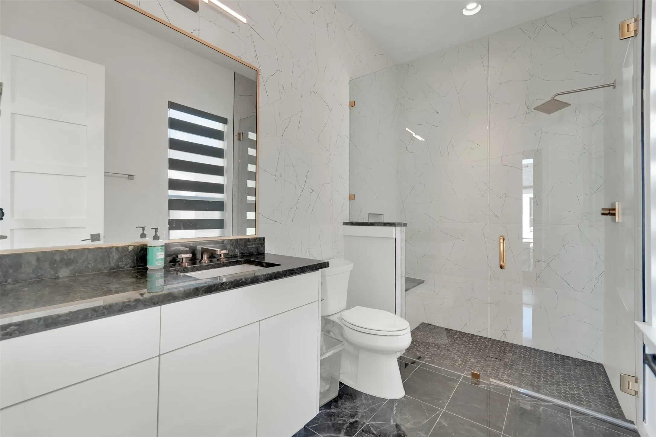 Vanity with dark stone countertop, undermount sink, and bronze-finish fixtures