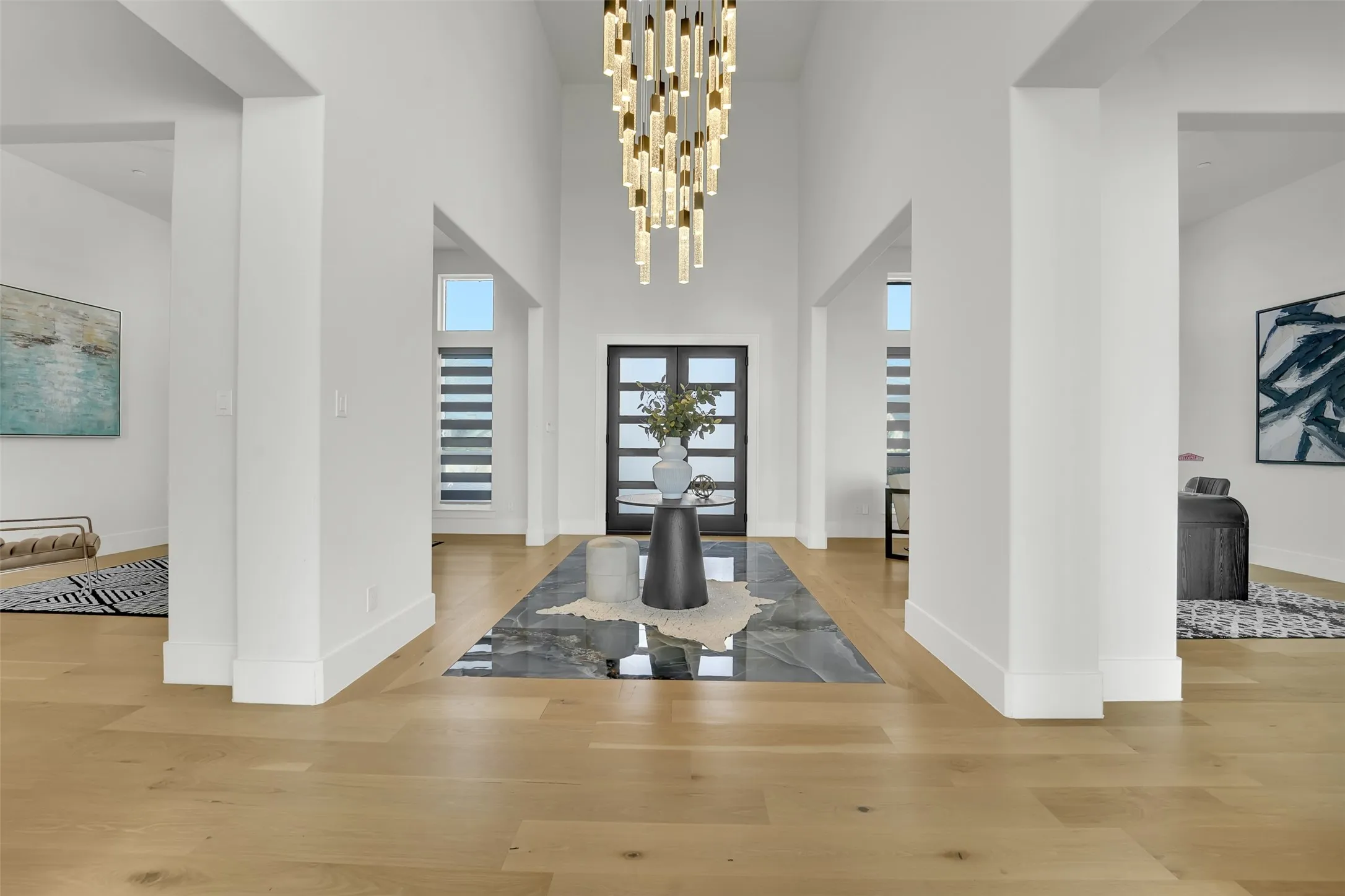 Double-height foyer featuring a contemporary chandelier, two-panel glass entry doors, and light wood-finish flooring