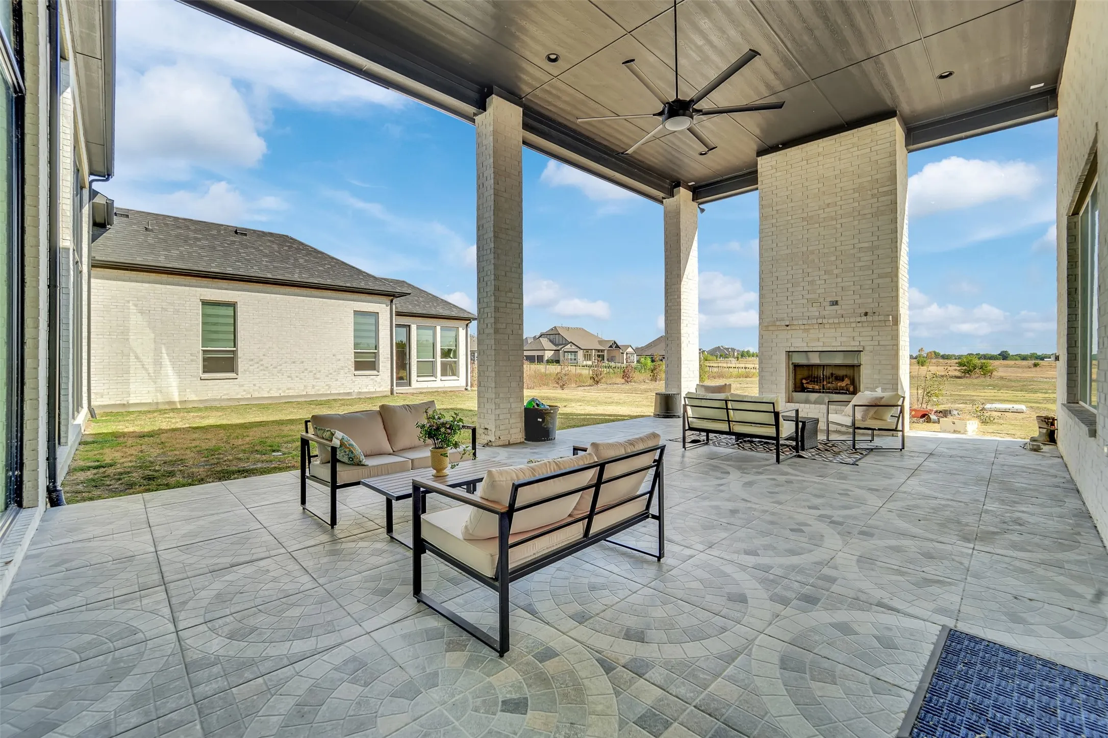 Expansive covered patio featuring a patterned concrete surface, full-height brick fireplace, and ceiling fan