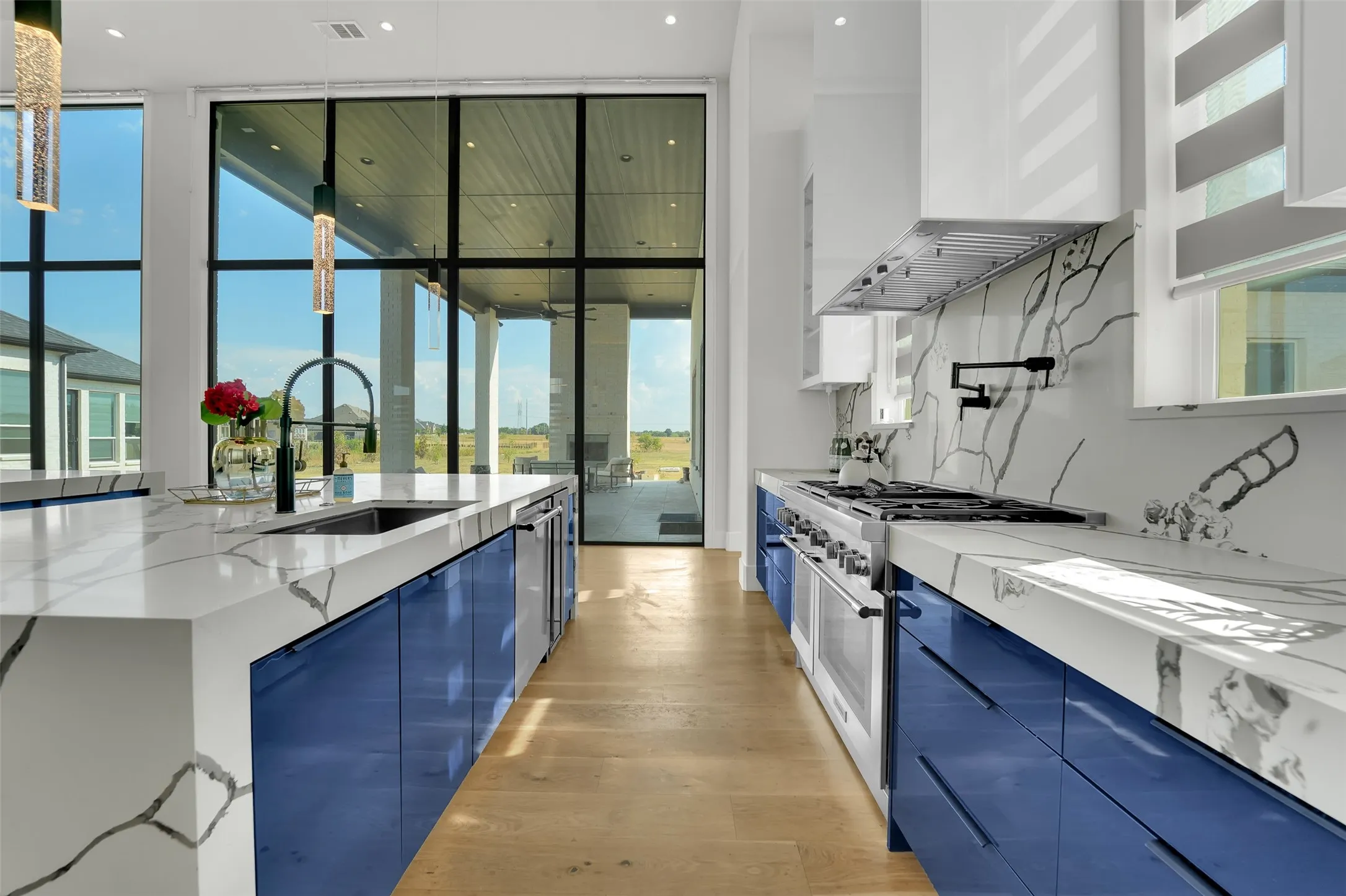 Expansive kitchen featuring a large island with an undermount sink, custom blue cabinetry, light wood-finish flooring, and a range oven with a coordinating hood