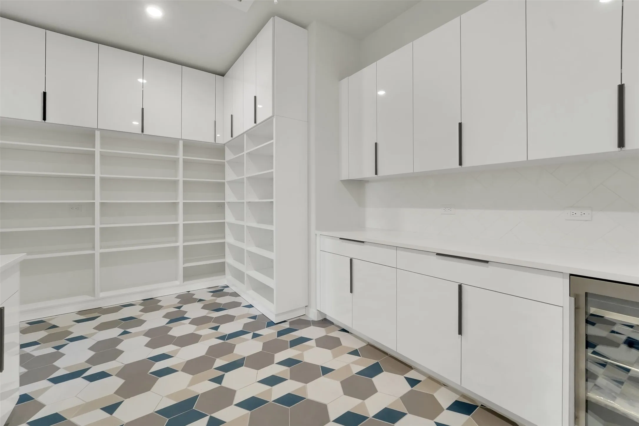 Extensive built-in shelving, white flat-panel cabinetry with matte black hardware, stone countertops, herringbone tile backsplash, and a wine refrigerator