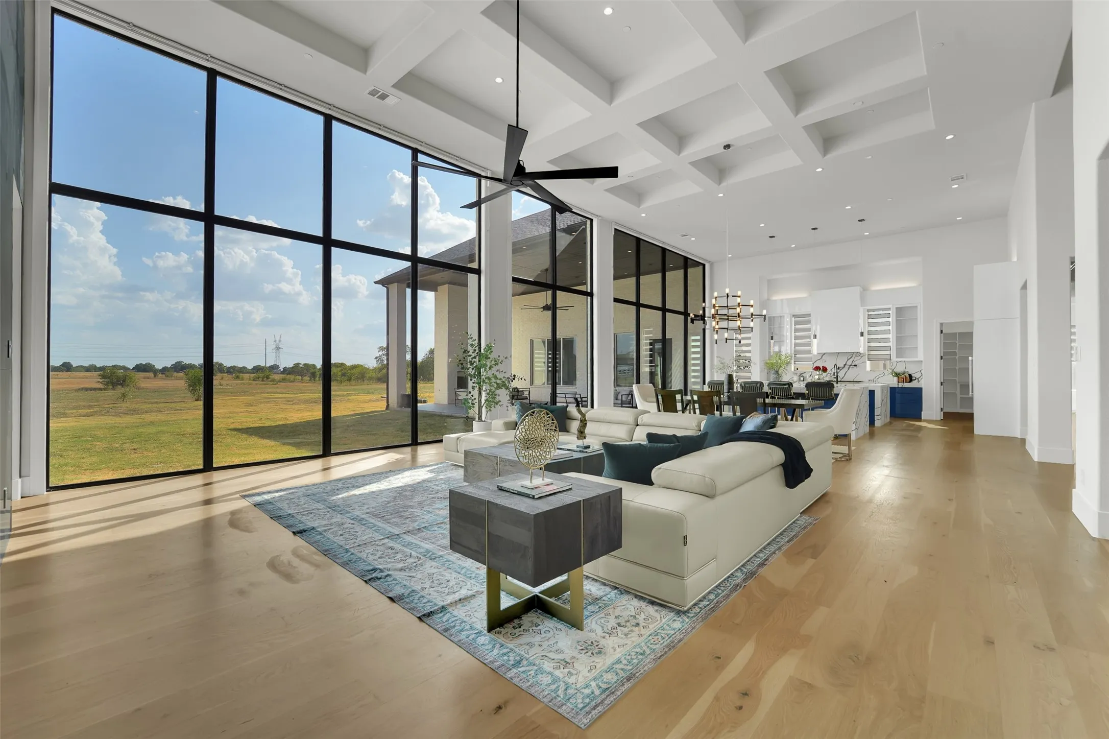 Expansive window wall with black framing, coffered ceiling, wood-finish flooring, open-concept design, and a modern ceiling fan
