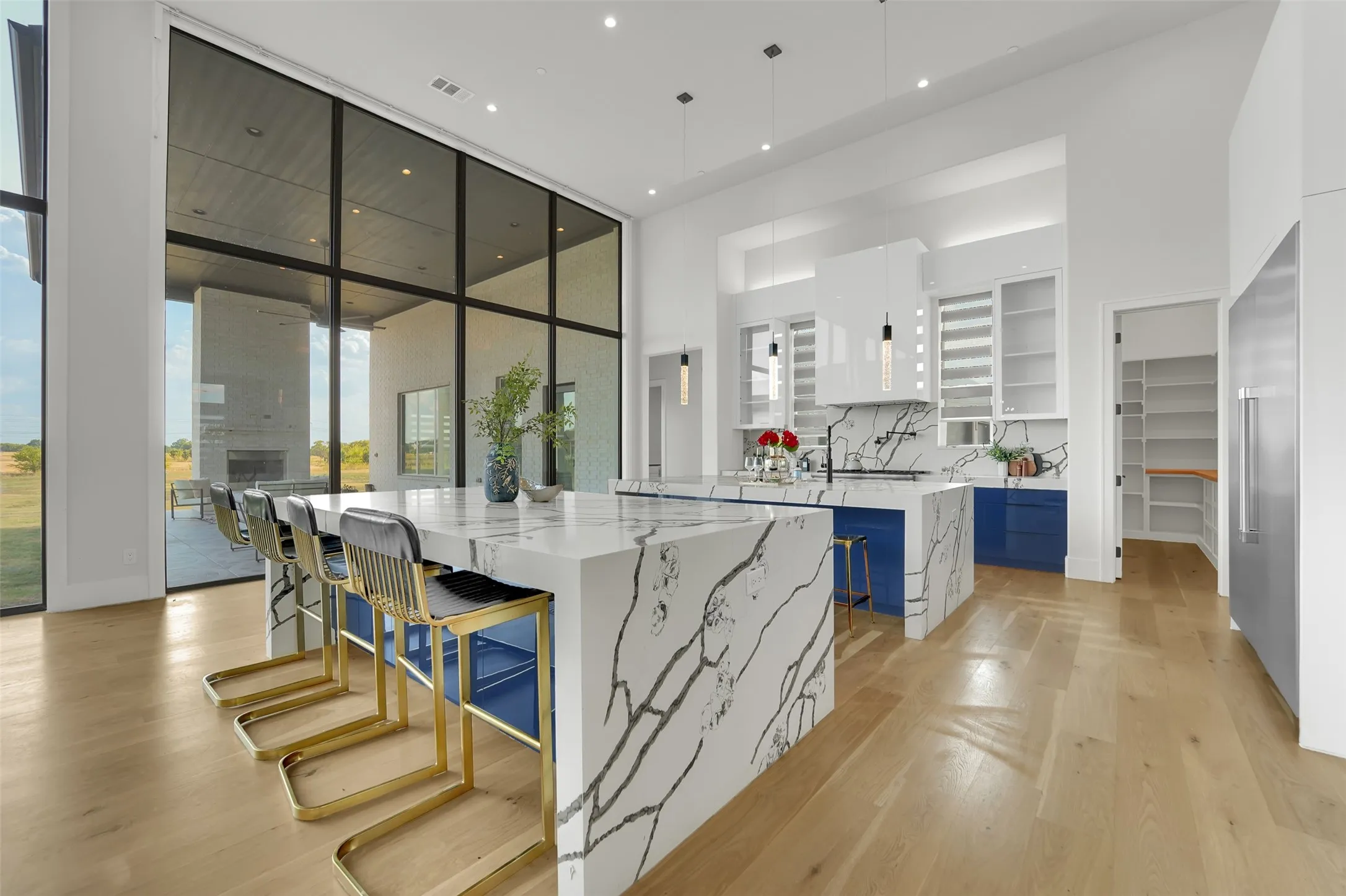 Vaulted ceilings, expansive window wall, light wood-finish flooring, and white and blue cabinetry with veined countertops