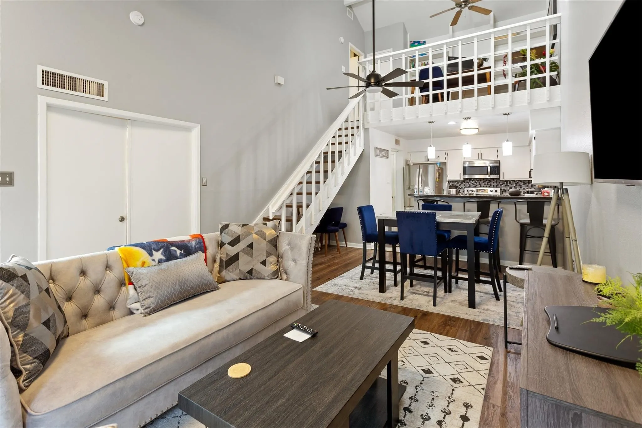 Vaulted ceiling living area with wood-finish flooring, staircase with white railings, and a loft overhead