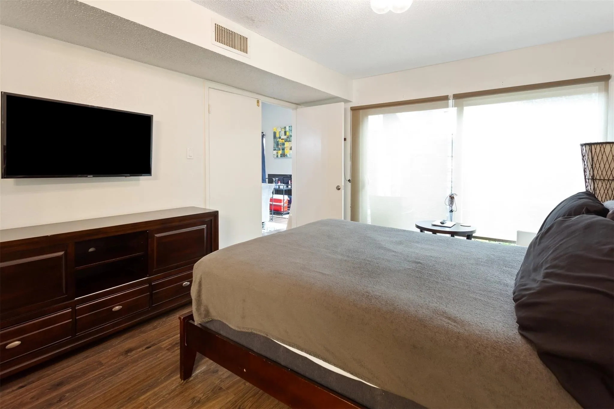 Bedroom 1 -Wood-finish flooring with a wall-mounted display, built-in media console, and large sliding glass door