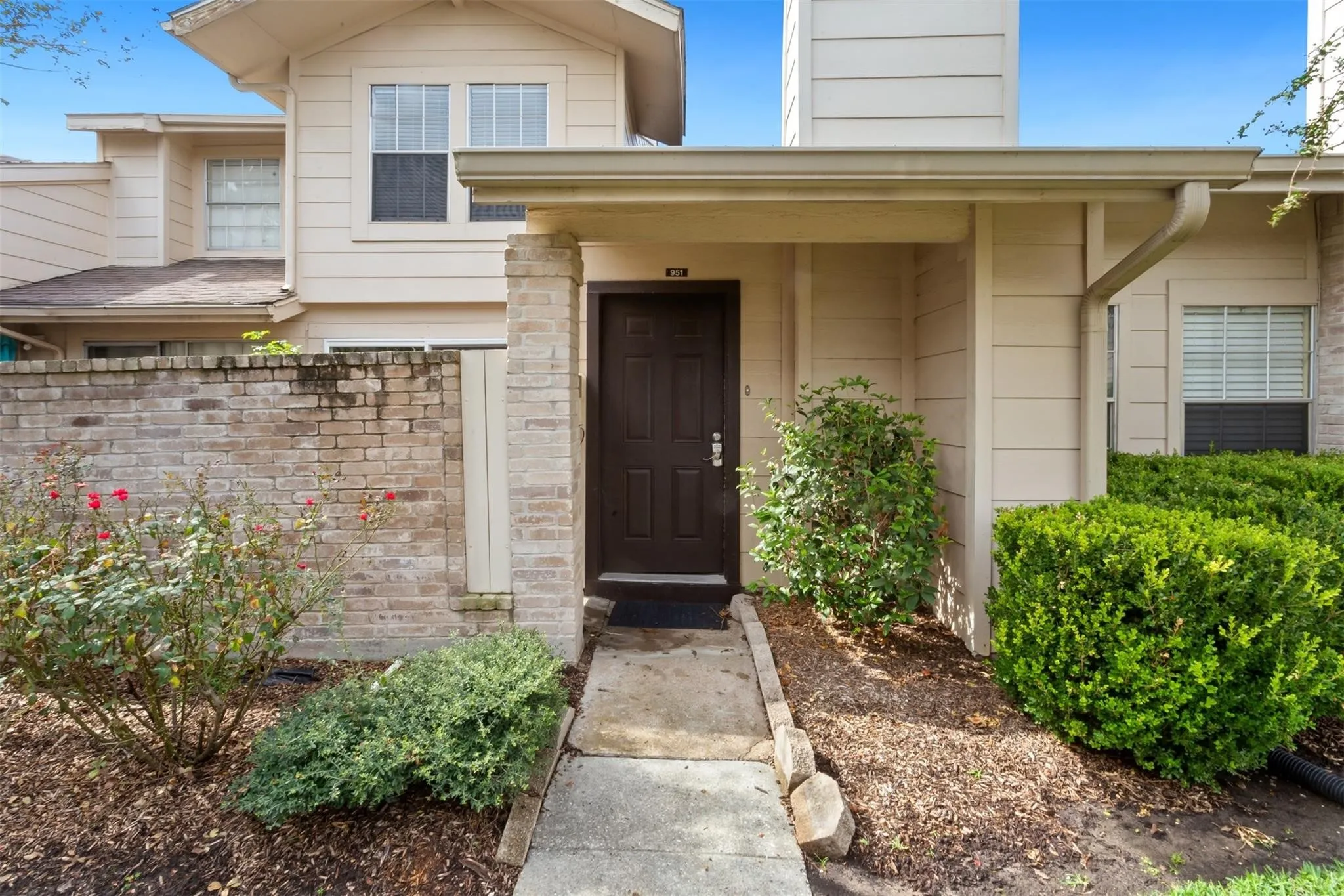 Entryway with a covered porch, brick column accents, and surrounding landscaping