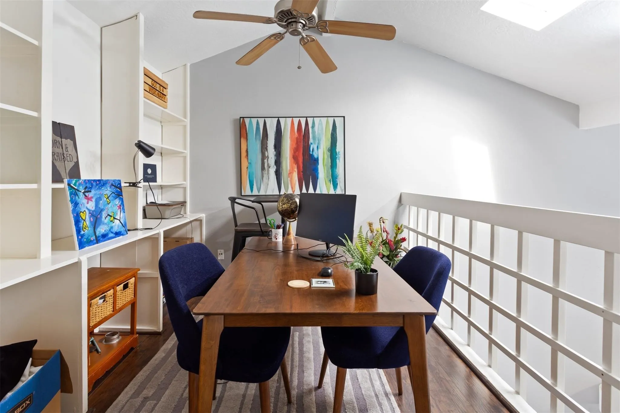 Vaulted ceiling with skylight, wood-finish flooring, built-in shelving, ceiling fan, and white railing
