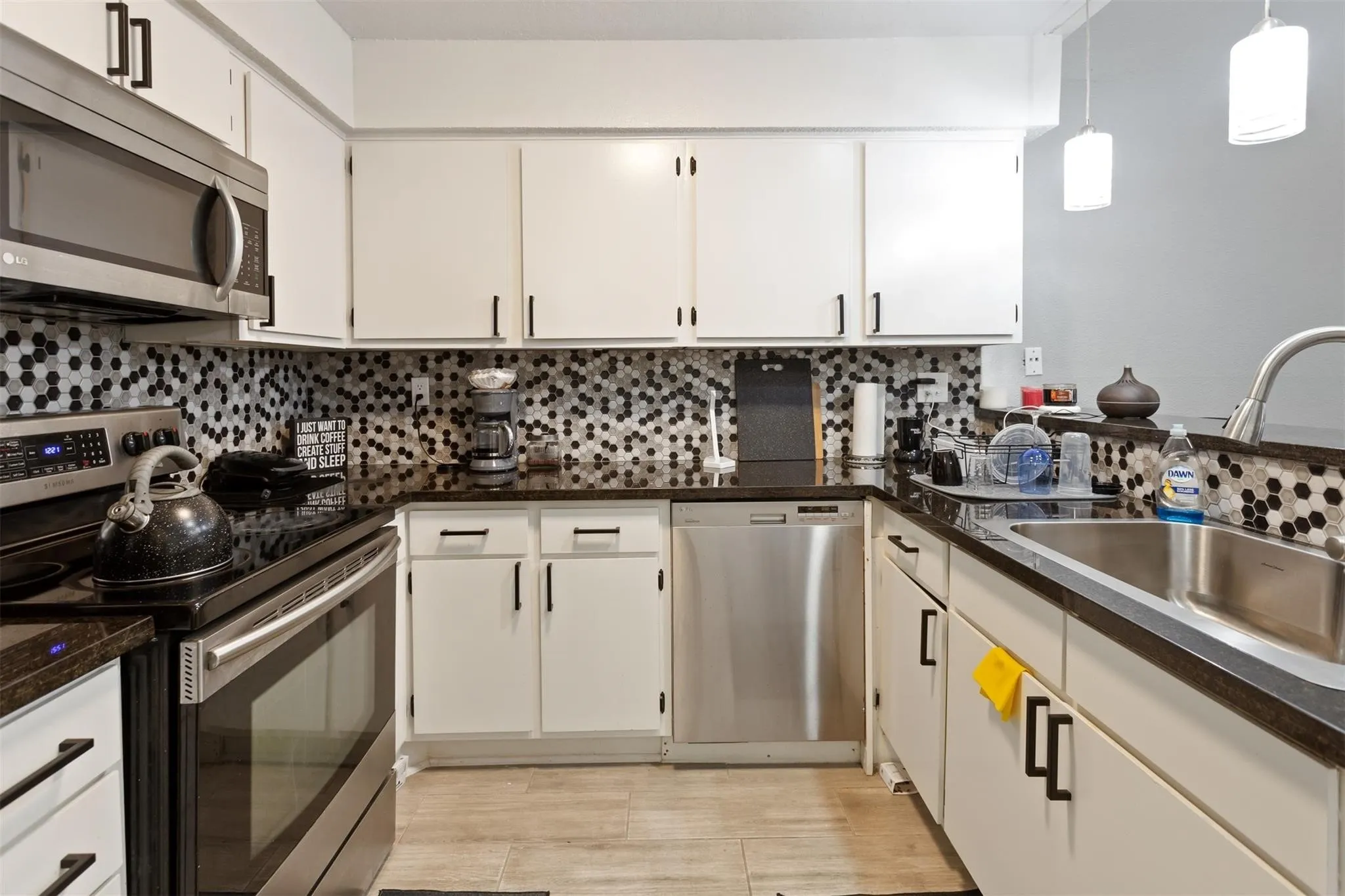 Kitchen featuring white cabinetry, dark countertops, a tiled backsplash, stainless steel appliances, and wood-finish flooring