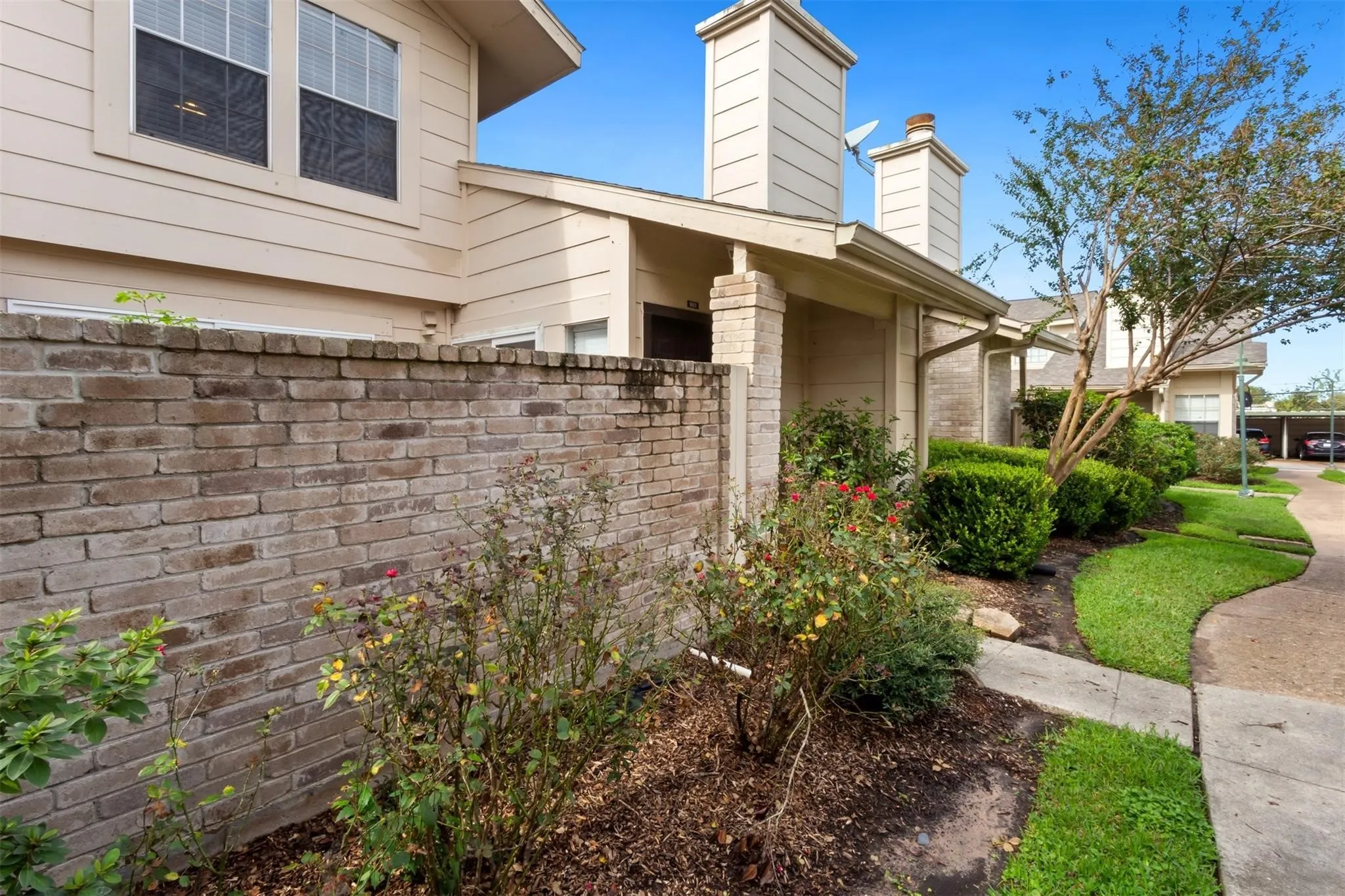 Brick fence with integrated landscaping, mature shrubs, and manicured lawn