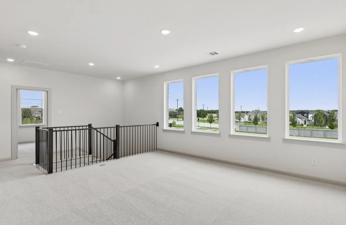 Spacious room with plush carpet flooring, recessed lighting, and a black wrought iron railing