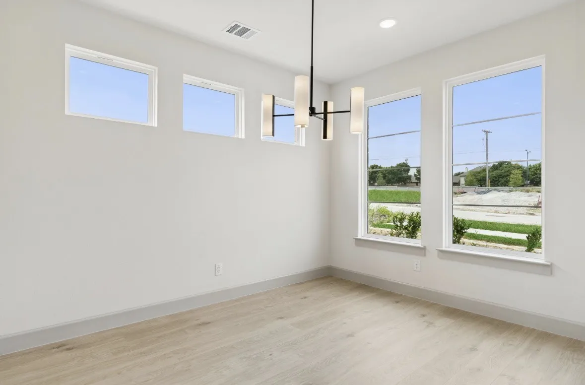 Spacious room featuring light wood-finish flooring, a contemporary ceiling light fixture, and multiple windows