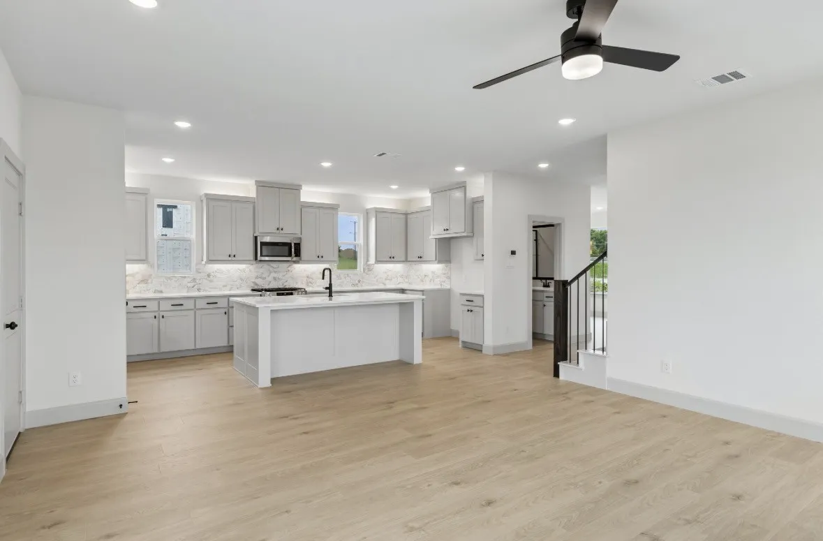 Kitchen featuring light-toned cabinetry, a central island with sink, stainless steel microwave, and white countertops with a matching backsplash