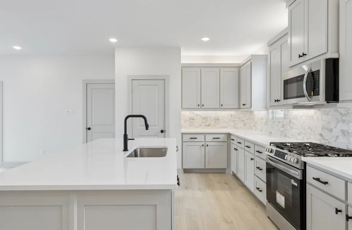 Kitchen featuring light-toned cabinetry, stainless steel appliances, a center island with sink, stone countertops, and a full tile backsplash