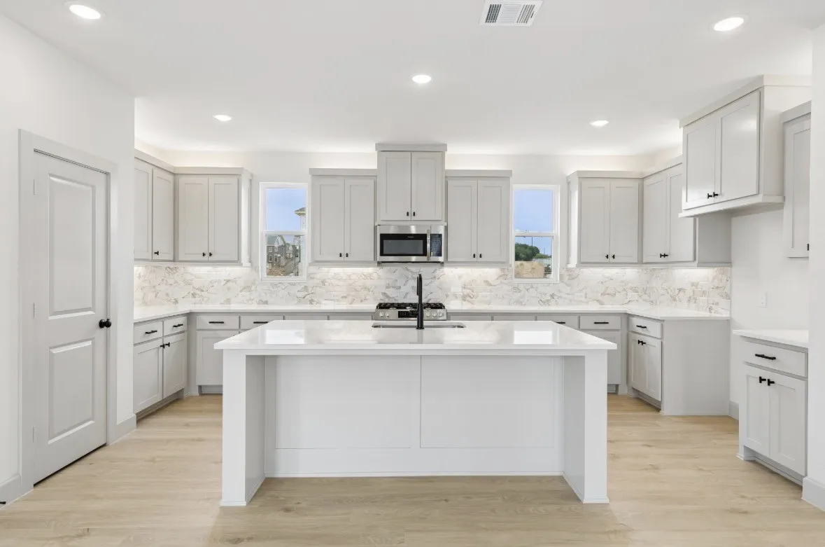 Kitchen featuring a central island, light-toned cabinetry, a full height backsplash, stainless steel appliances, and wood-finish flooring