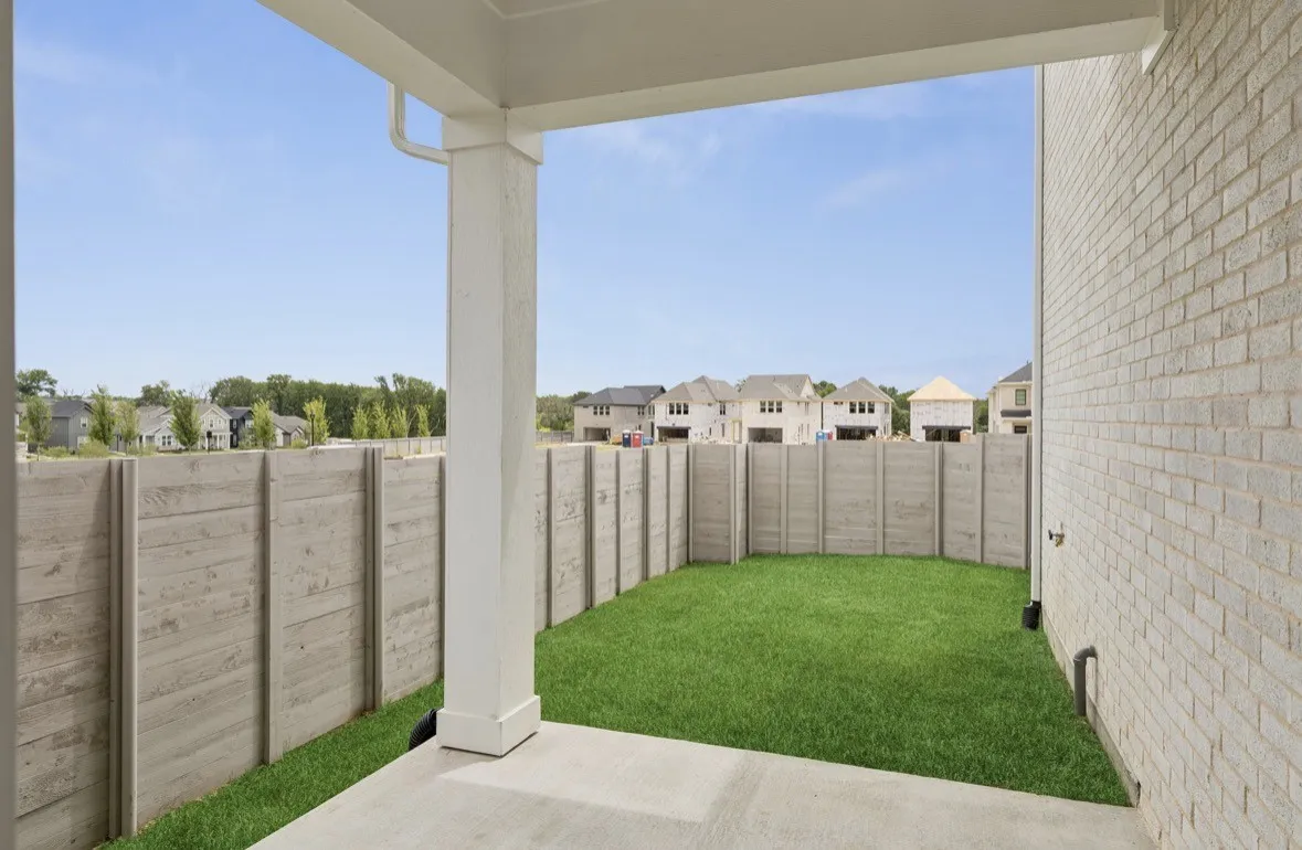 Covered concrete patio with white support column, leading to a fenced yard with established lawn