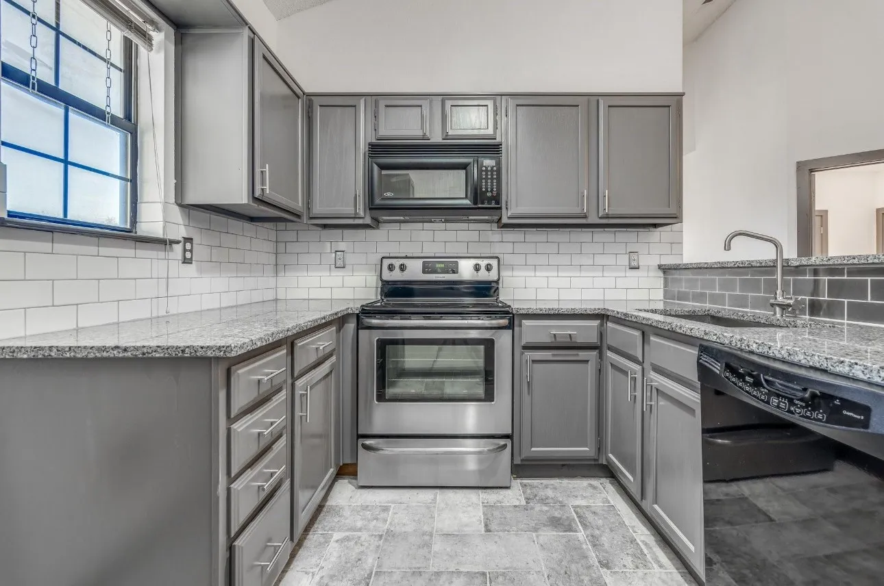 Kitchen with gray cabinetry, sink, light stone counters, and black appliances