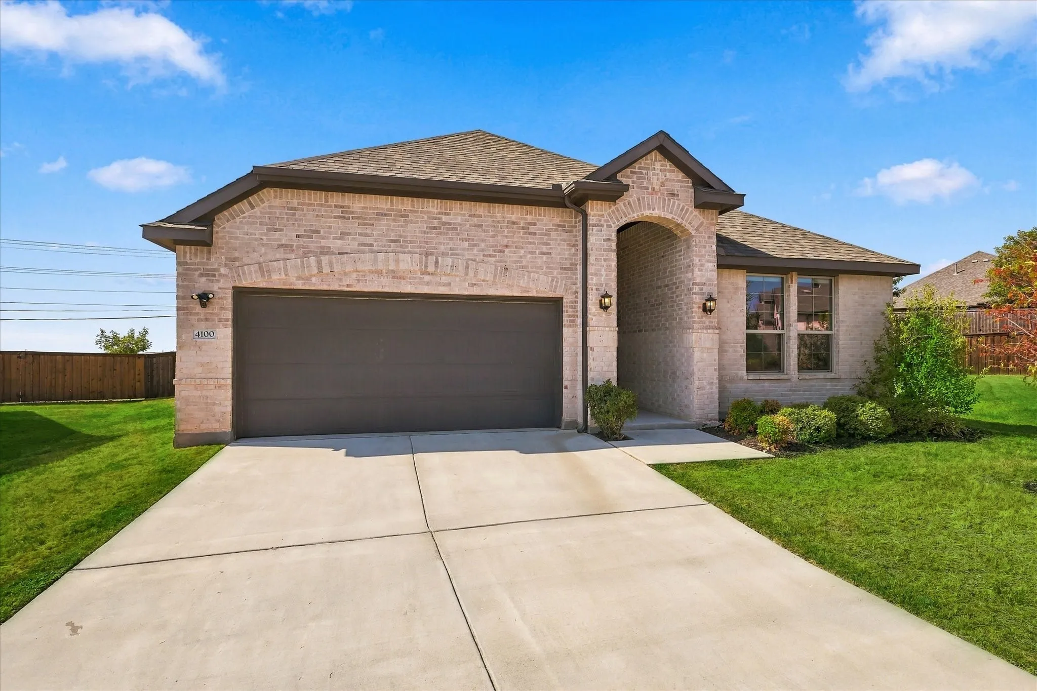 Brick exterior with a dark garage door, arched entryway, and dual exterior sconces