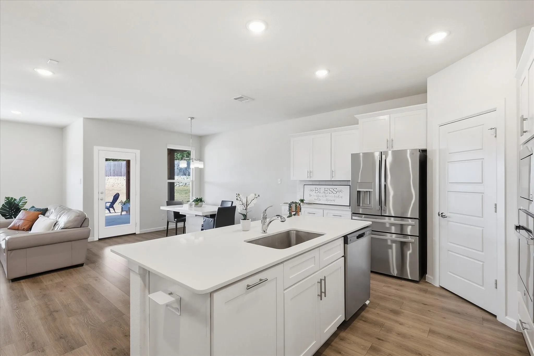 Open-concept living space with wood-finish flooring, recessed lighting, white cabinetry, stainless steel appliances, and a kitchen island with an undermount sink