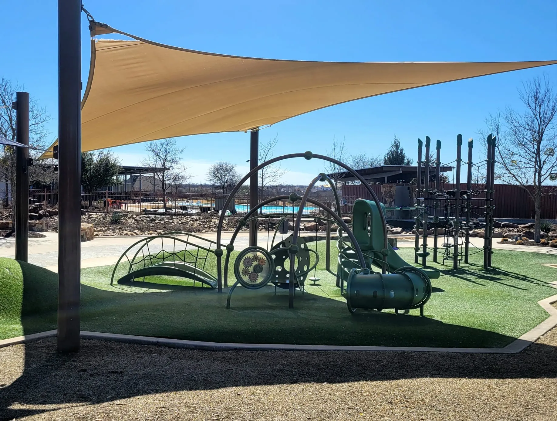 Playground featuring a shade sail, synthetic turf surfacing, and a variety of play structures
