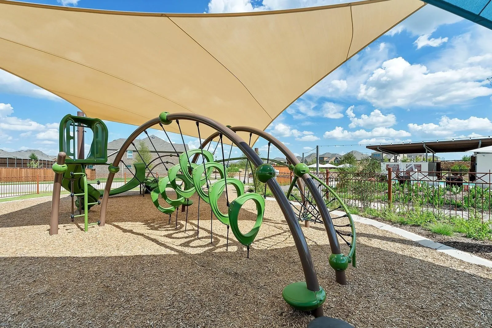 Playground area featuring a shade structure, wood chip ground cover, and adjacent walking path