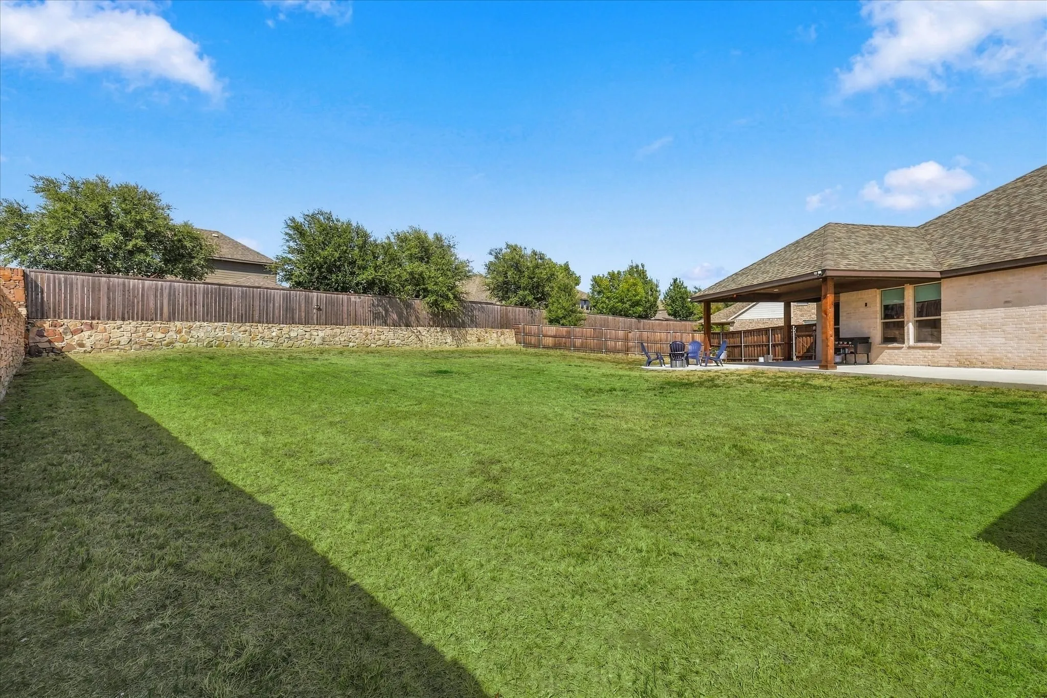 Expansive manicured lawn with a covered patio featuring wood support columns
