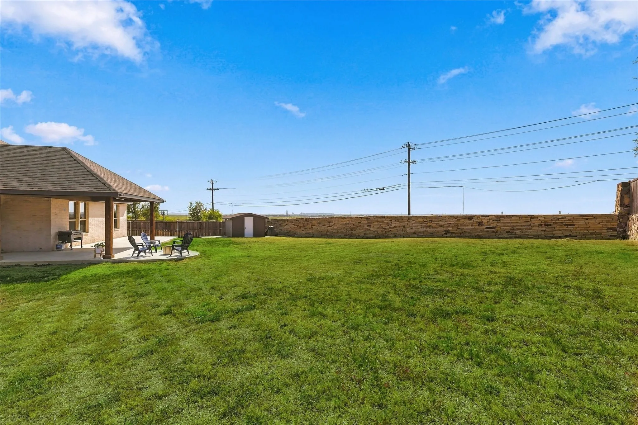 Expansive green lawn with a covered patio area and a separate storage shed