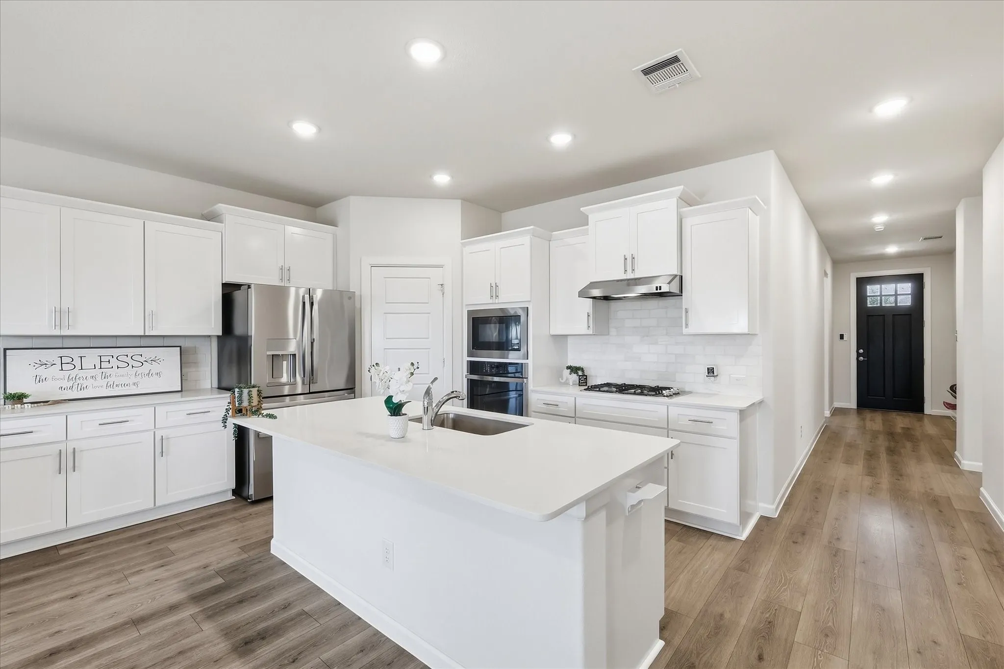 Kitchen featuring white cabinetry, stainless steel appliances, a center island with an undermount sink, recessed lighting, and wood-finish flooring