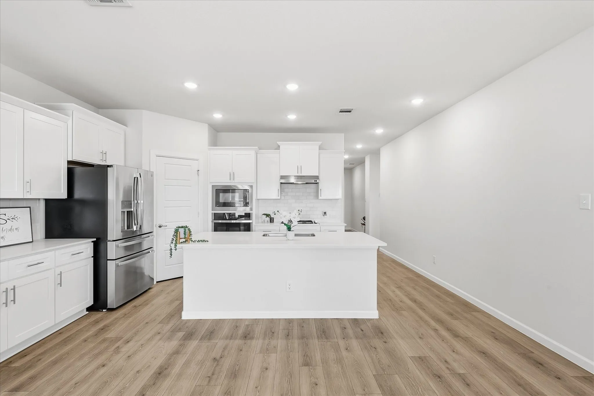 Open-concept kitchen with a central island, stainless steel appliances, white cabinetry, recessed lighting, and wood-finish flooring