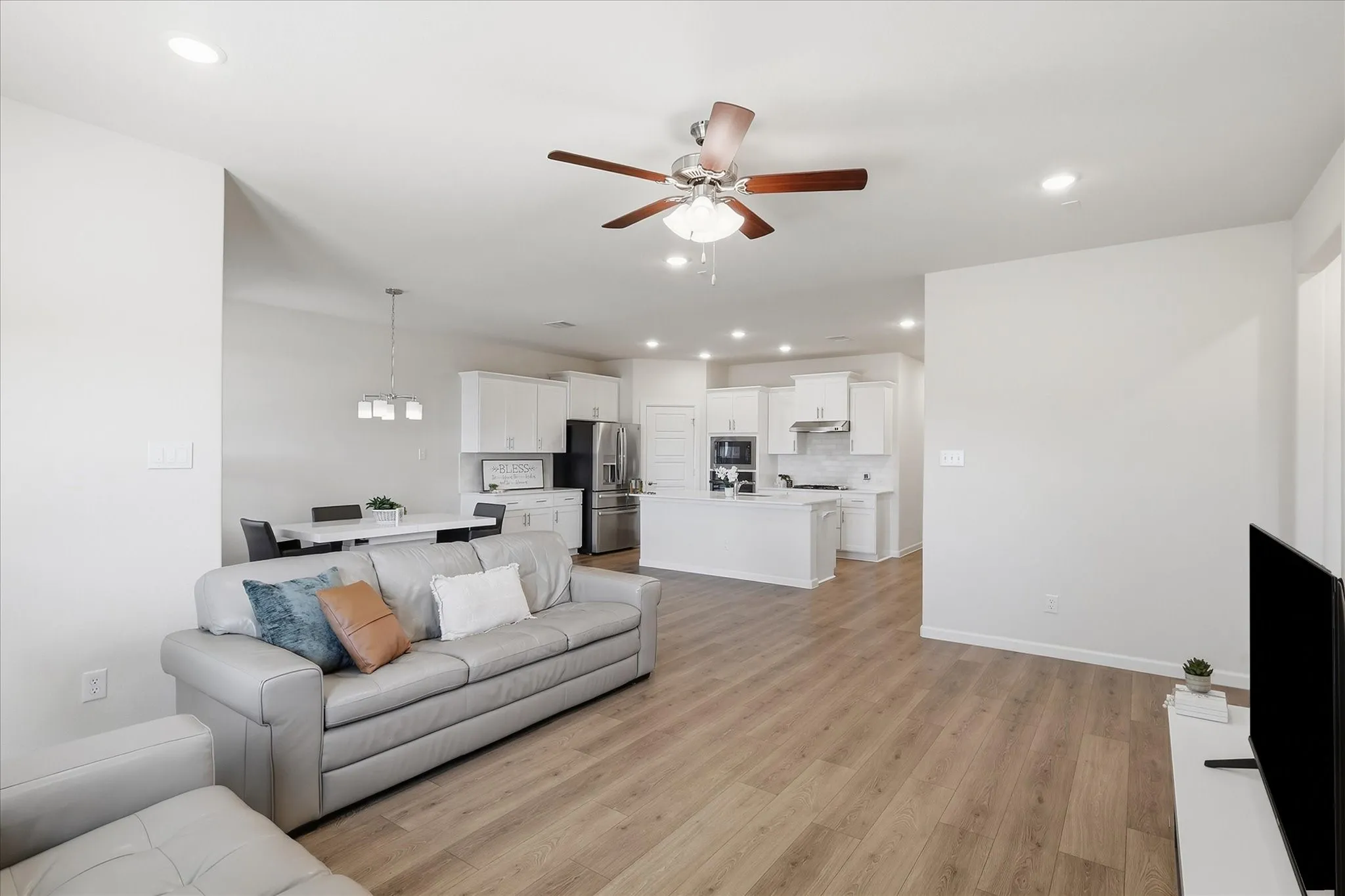 Recessed lighting, wood-finish flooring, ceiling fan, white cabinetry, and stainless steel appliances