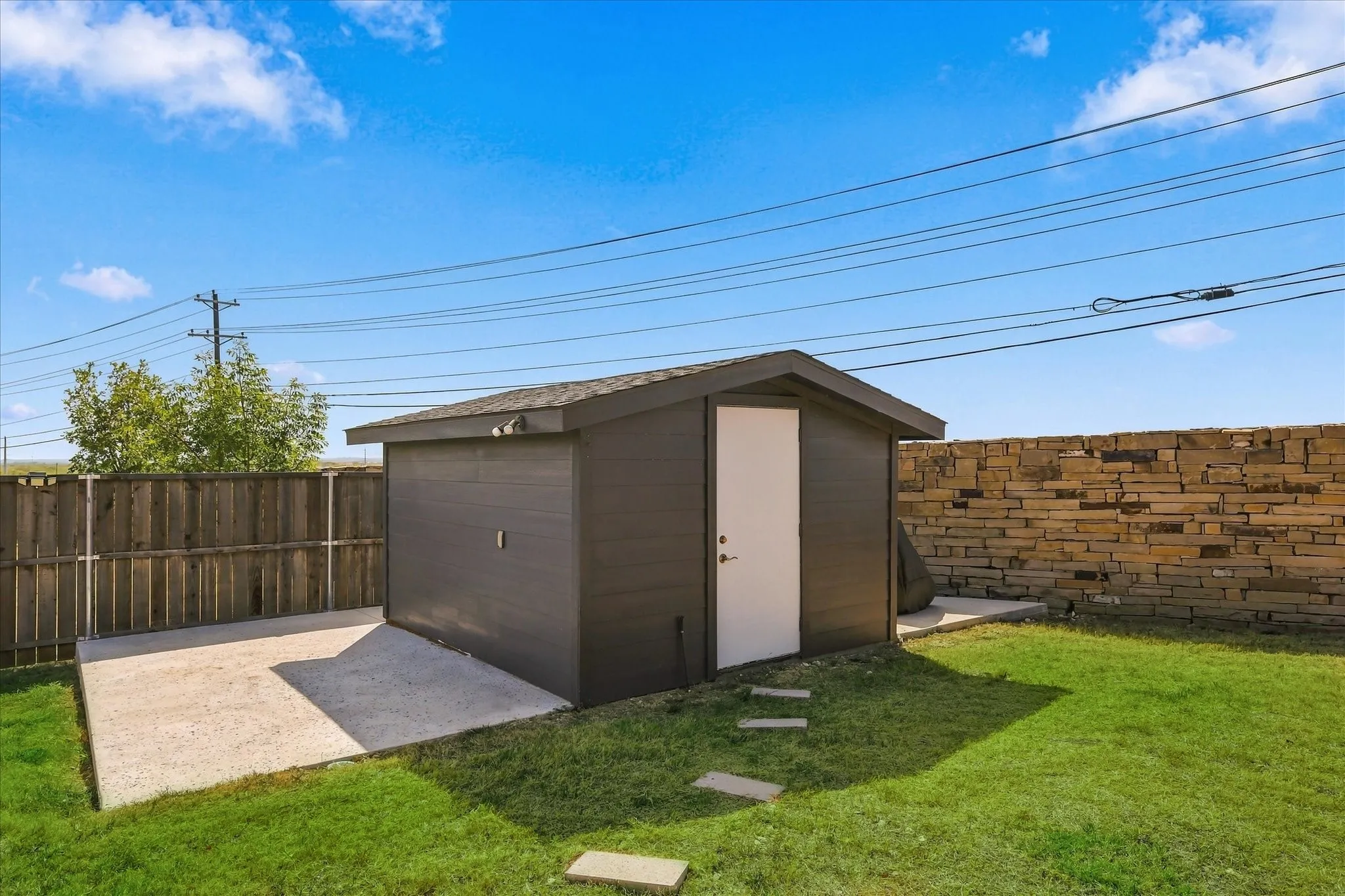 Landscaped backyard featuring a storage shed, concrete patio area, and stone wall