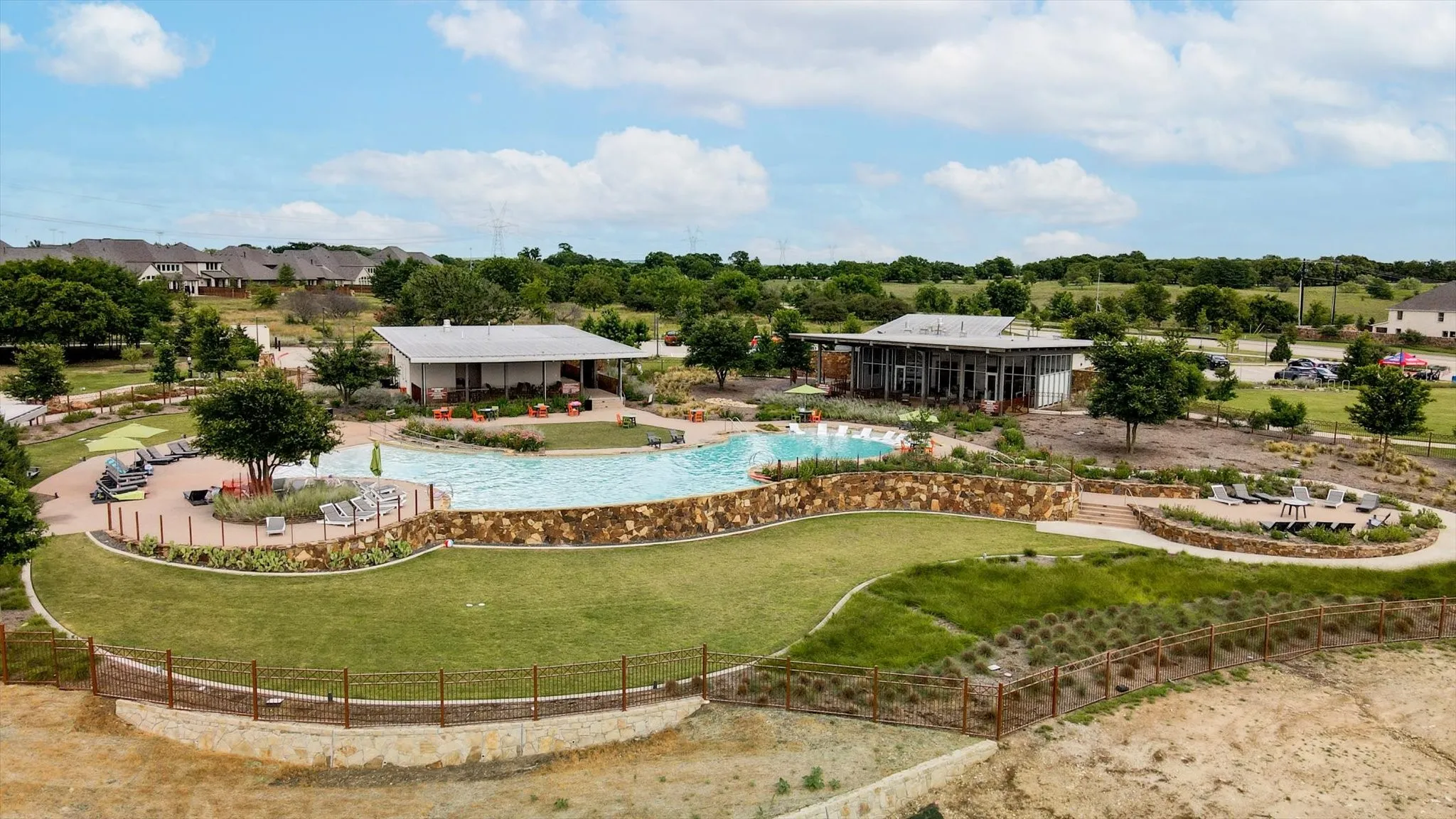 Expansive community pool with surrounding paved lounging areas, stone retaining walls, and landscaped grounds