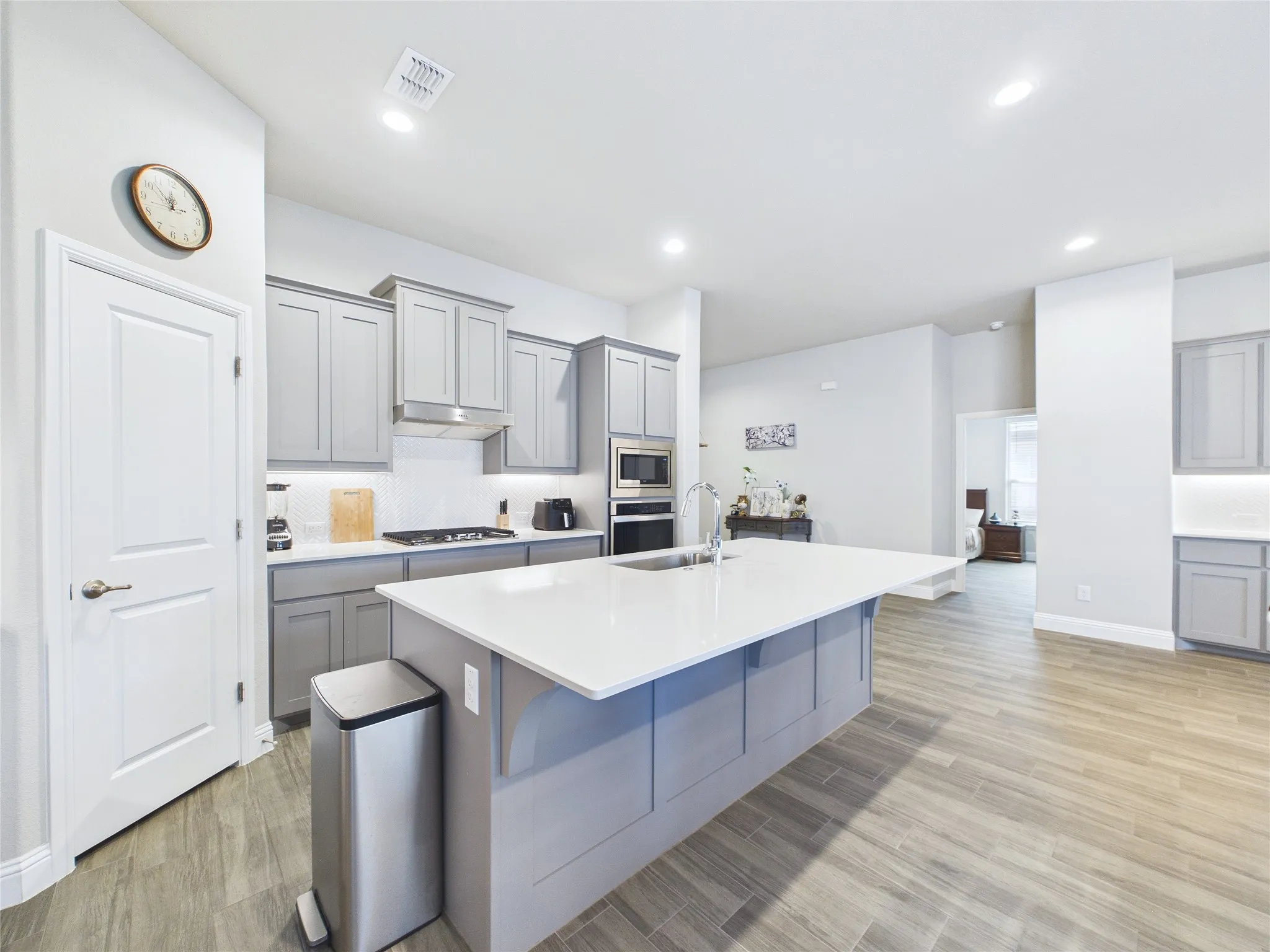 Kitchen featuring wood-finish flooring, an island with an undermount sink, gray cabinetry, built-in microwave, and a gas range