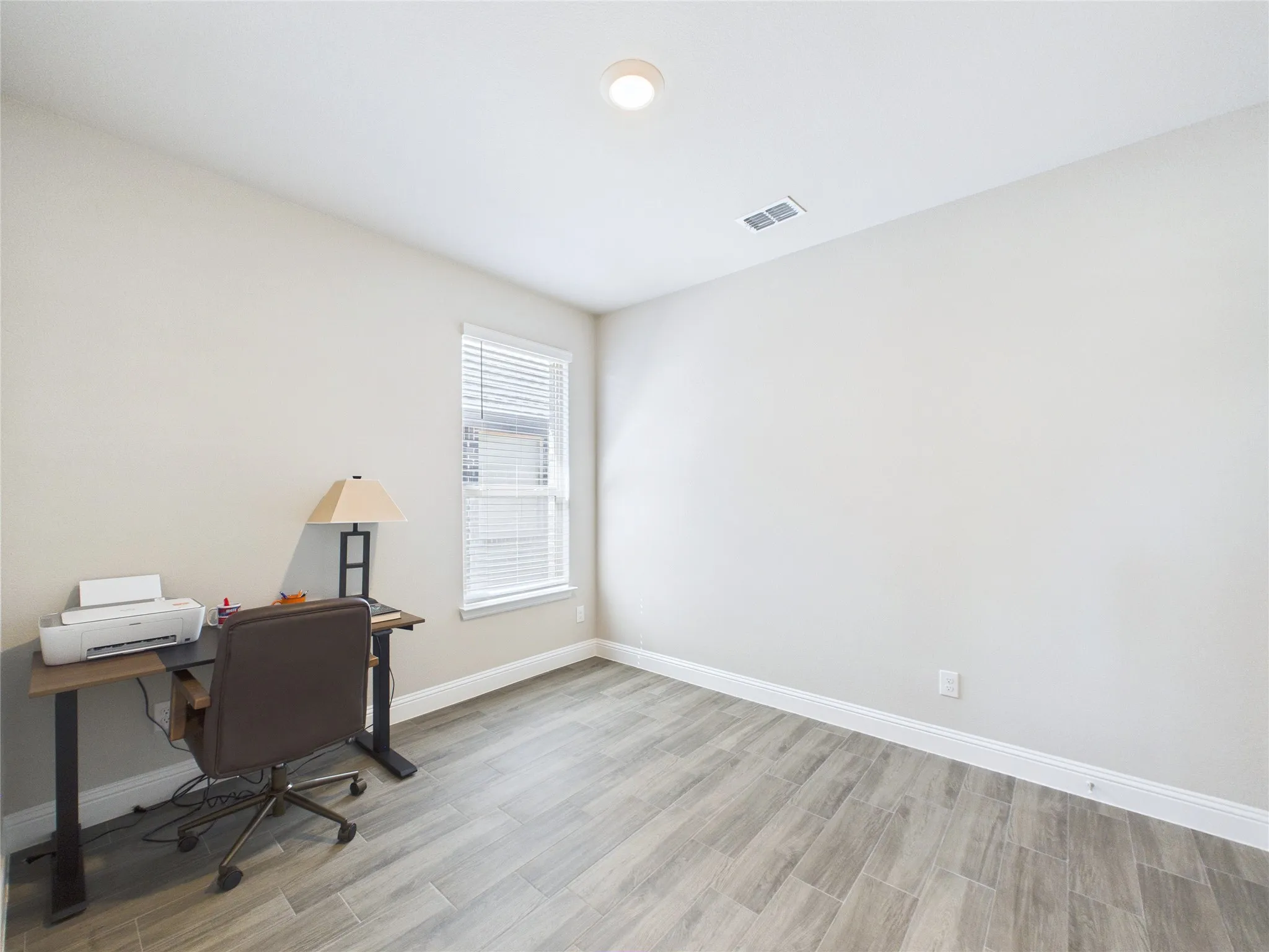 Neutral wall paint, wood-look flooring, ceiling-mounted light fixture, window with blinds