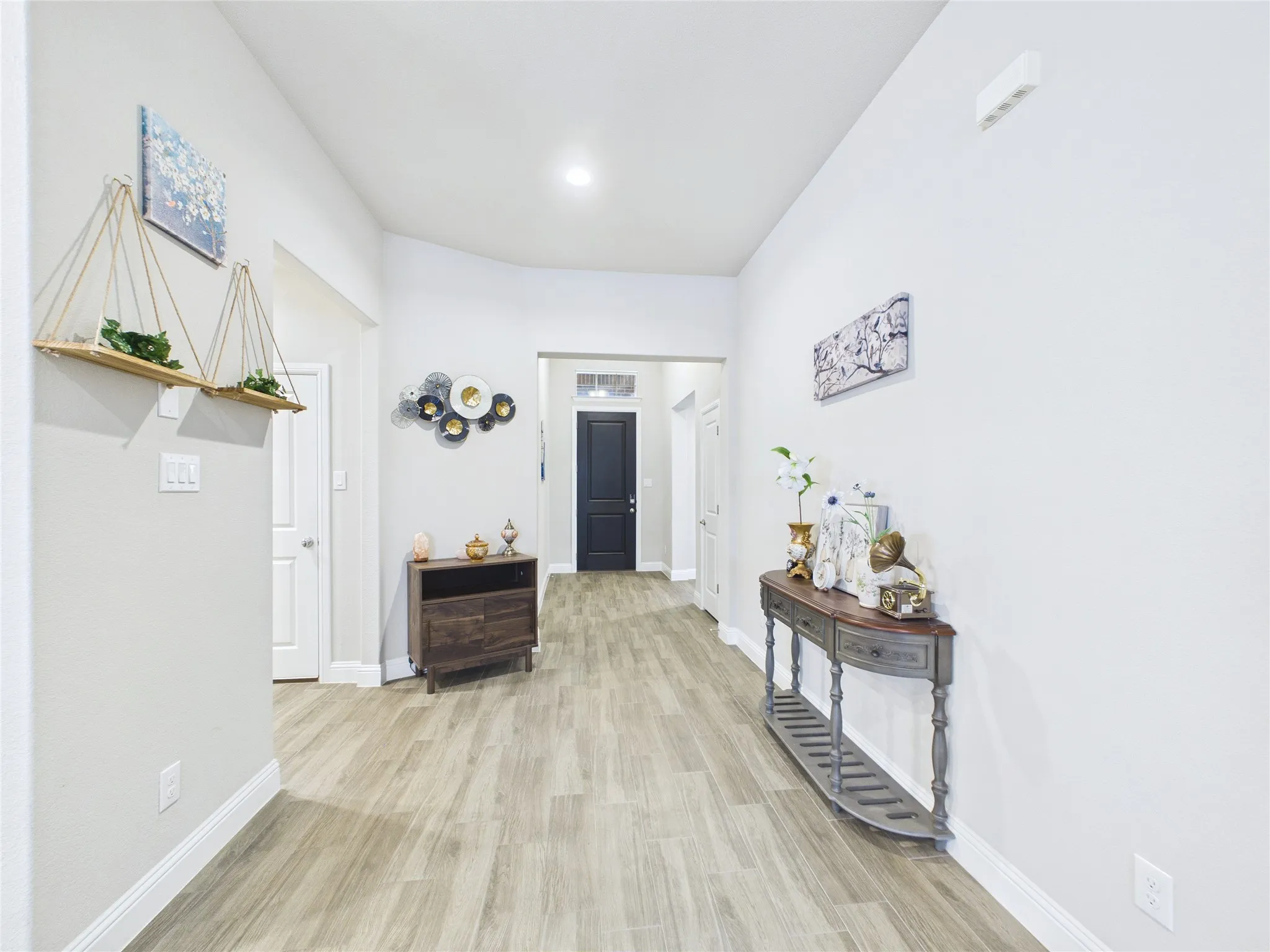 Recessed lighting illuminates the entrance hall featuring wood-finish flooring and a dark-paneled front door