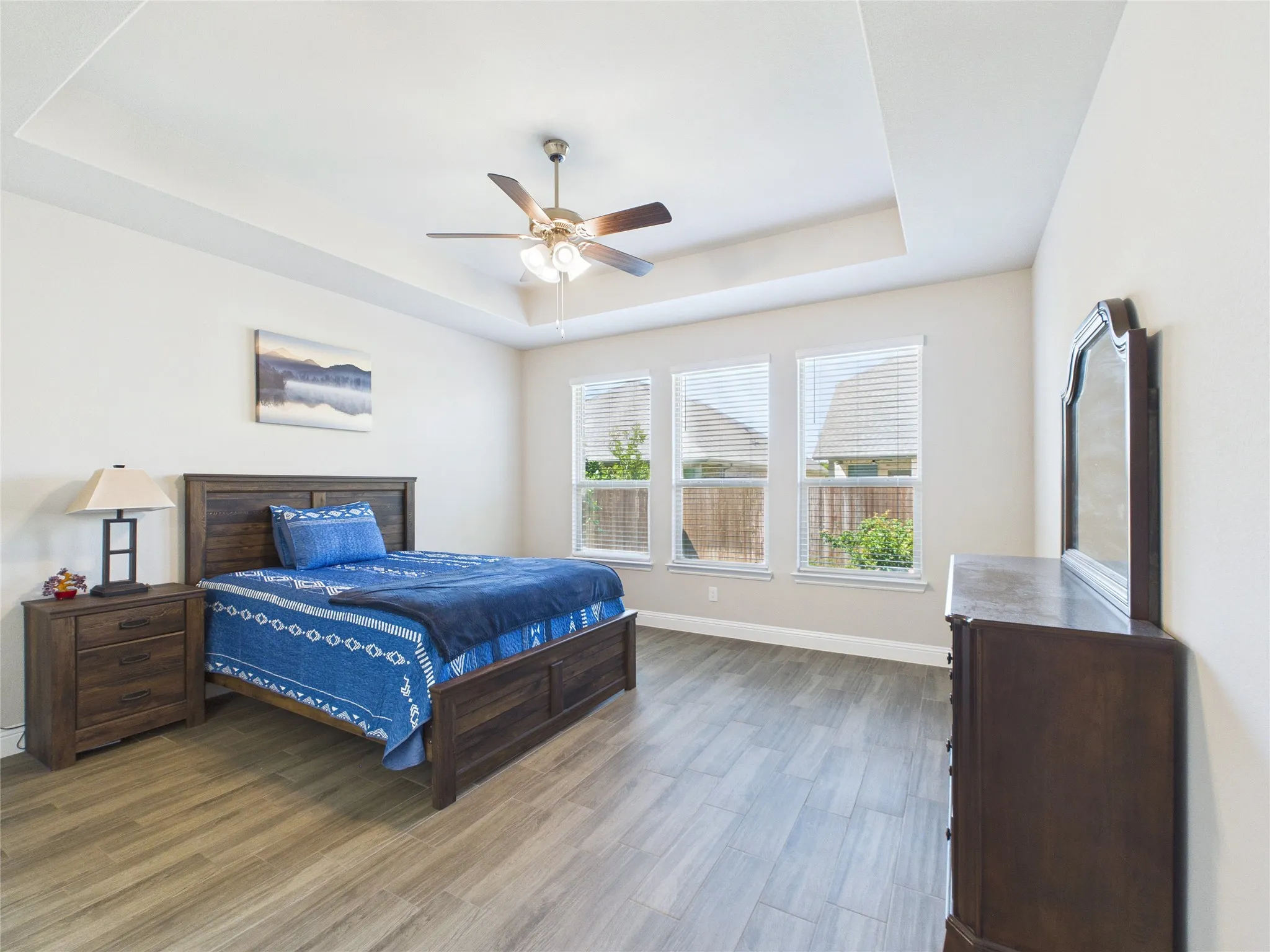 Recessed ceiling with a ceiling fan, three windows with blinds, and wood-finish flooring