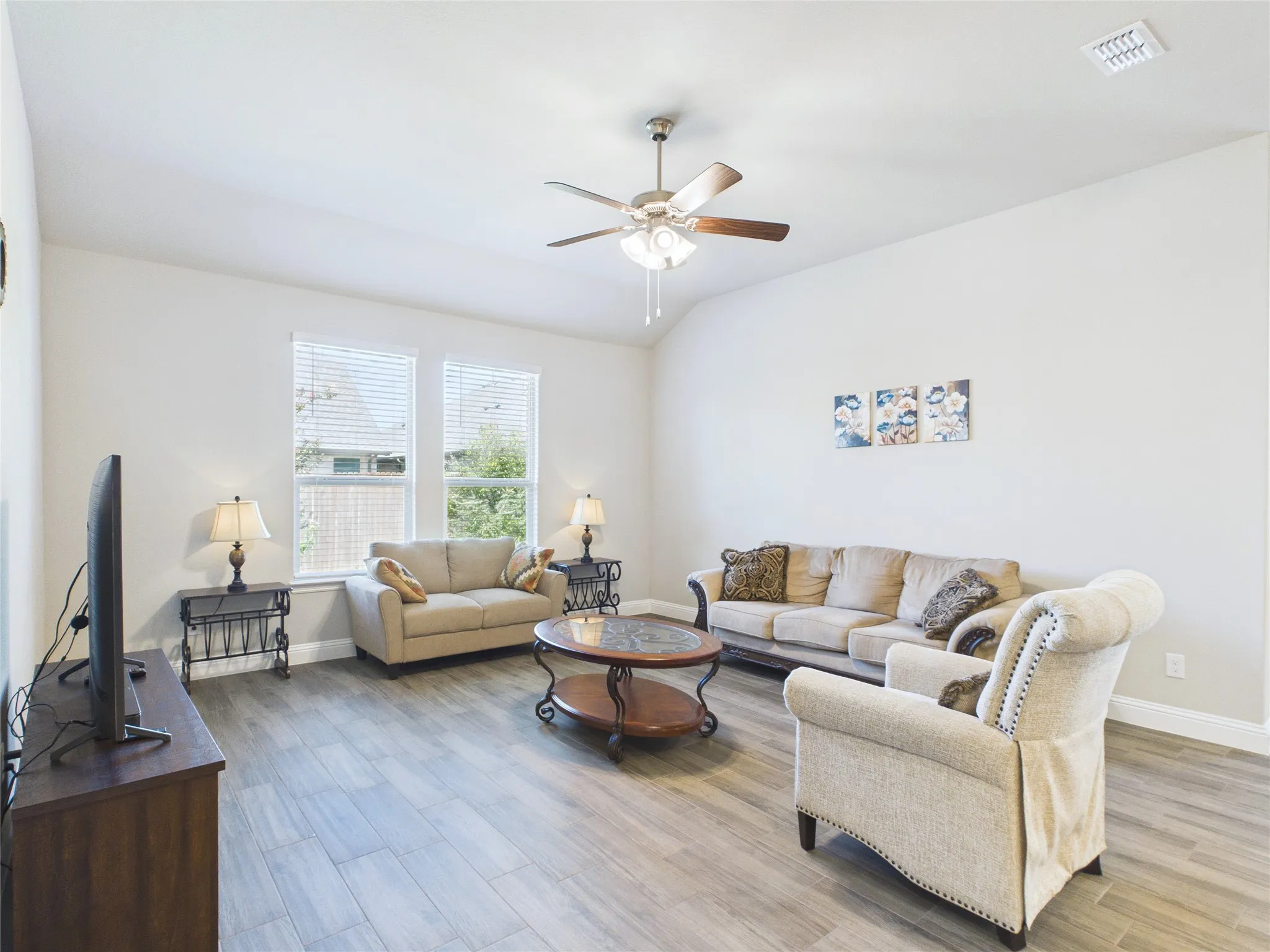 Vaulted ceiling with a ceiling fan, wood-finish flooring, and multiple windows with blinds