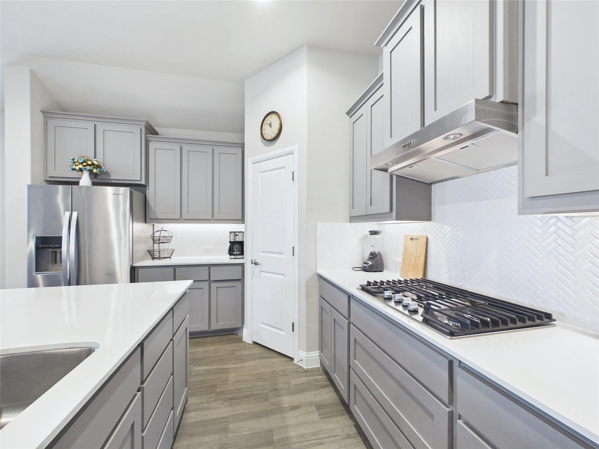Gray cabinetry, white countertops, stainless steel appliances, herringbone tile backsplash, and wood-finish flooring